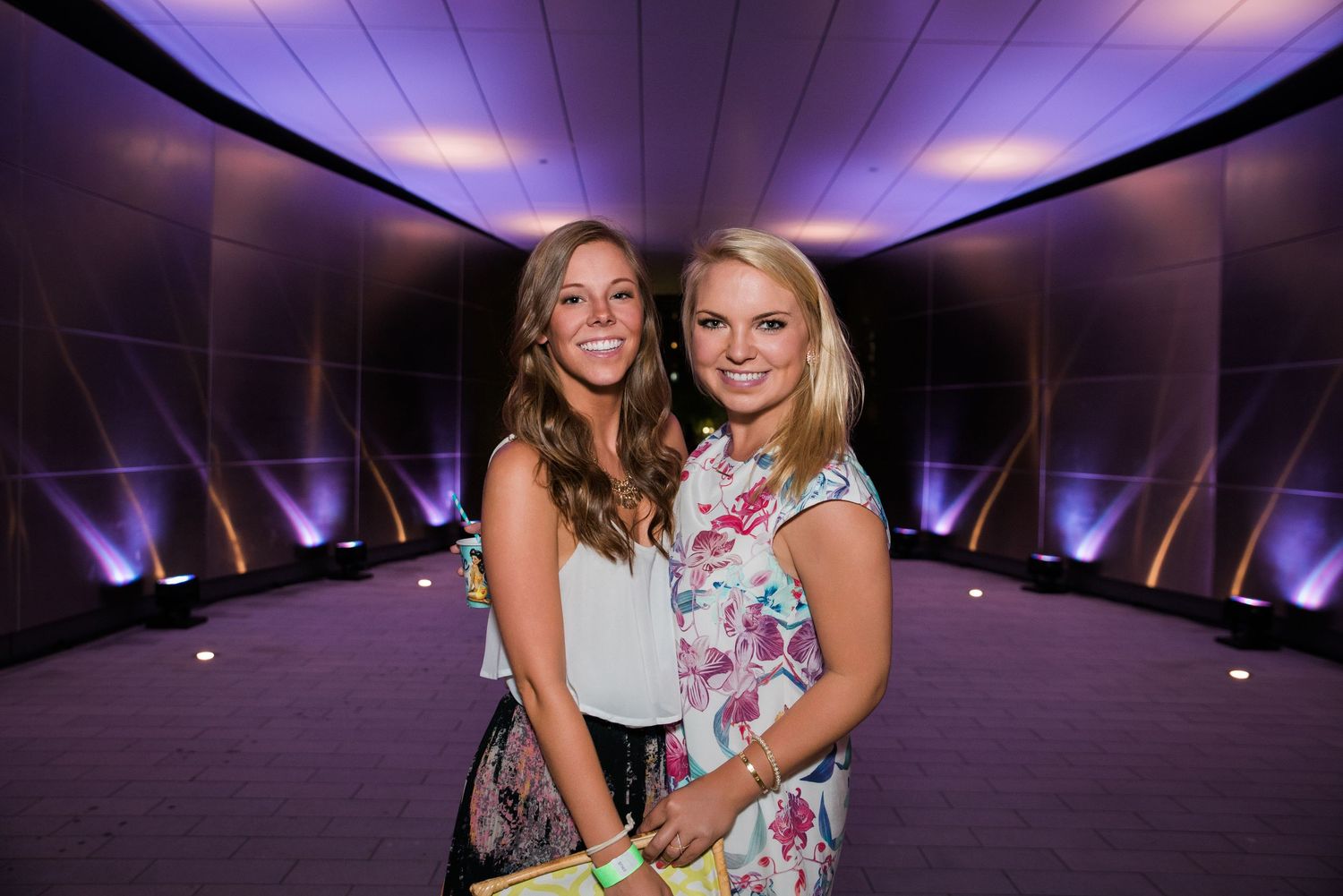 Two people posing in a purple-lit hallway at an evening event.