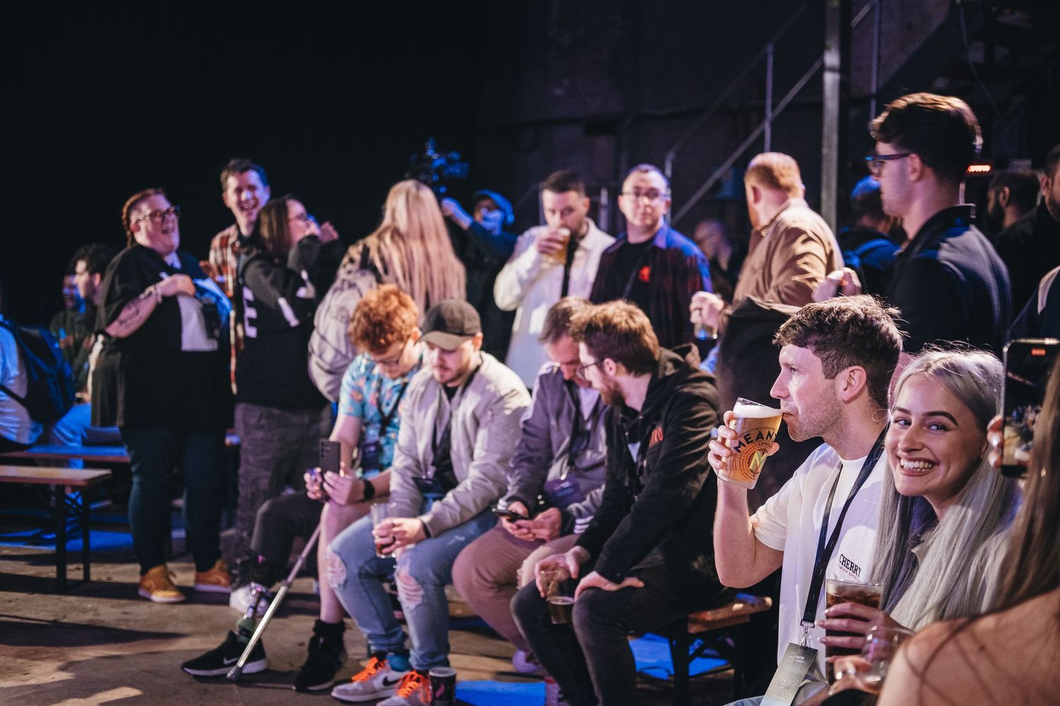 Audience sitting in blue chairs watching an entertainment event in a dark venue.