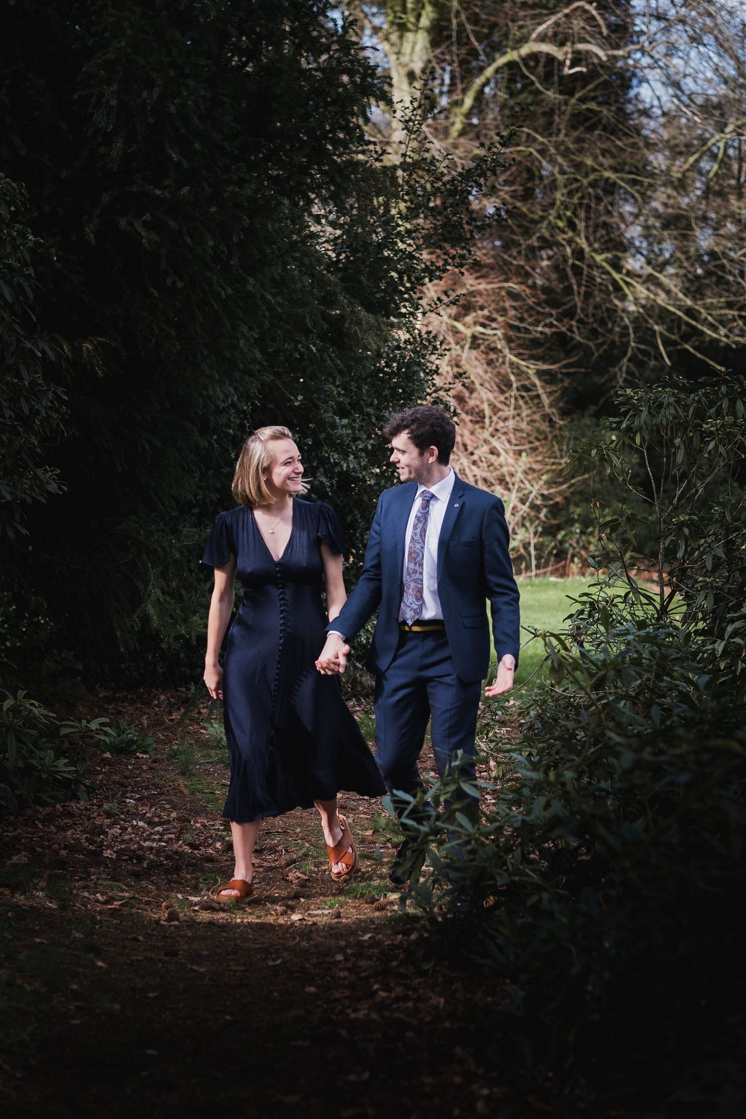 Couple walking through a dark wooded path in formal attire.
