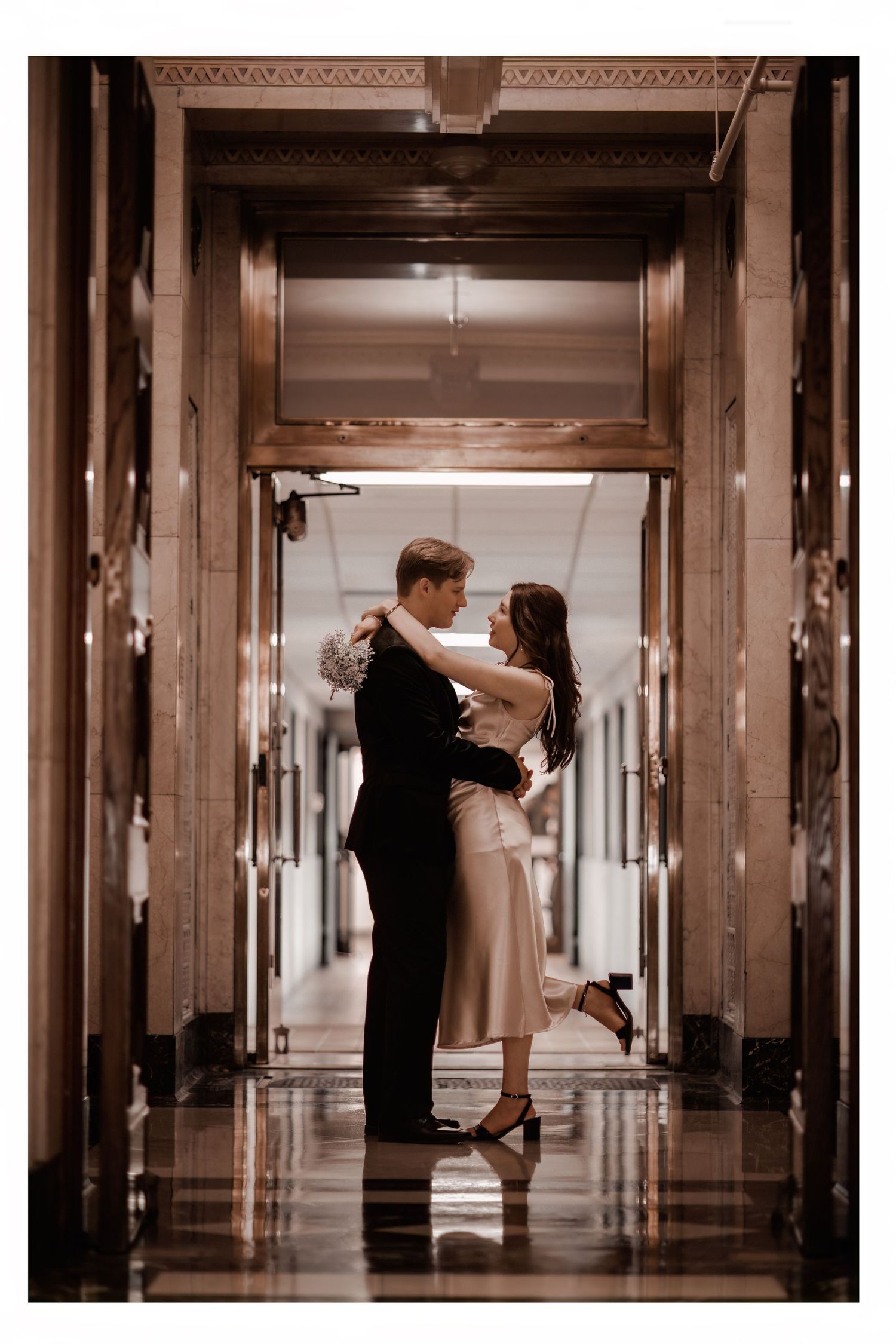 A romantic couple dances intimately in an elegant court house hallway with warm vintage lighting and reflective marble floors. Elopement.
