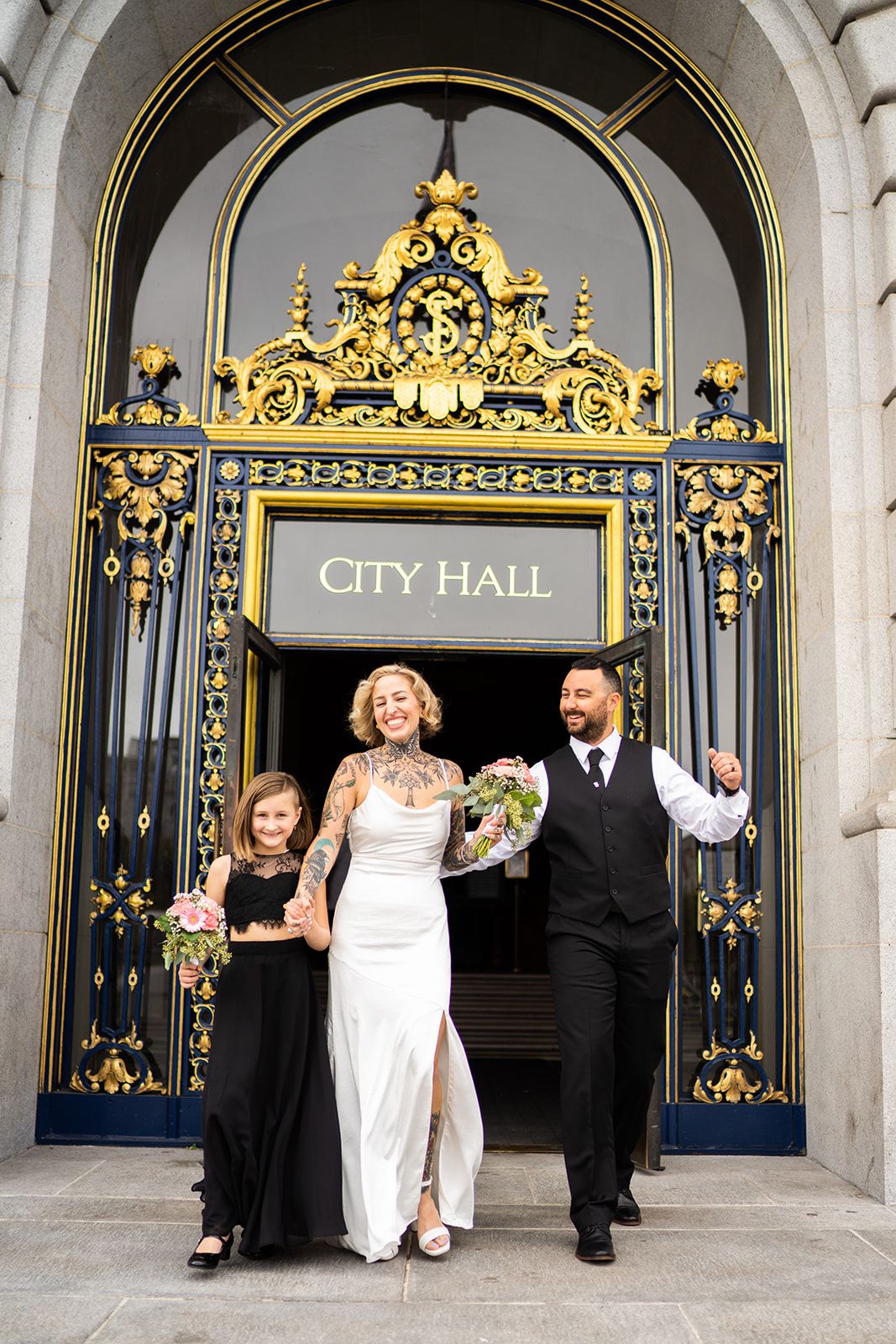 Wedding party exits ornate City Hall doors with decorative golden arch and intricate metalwork.
