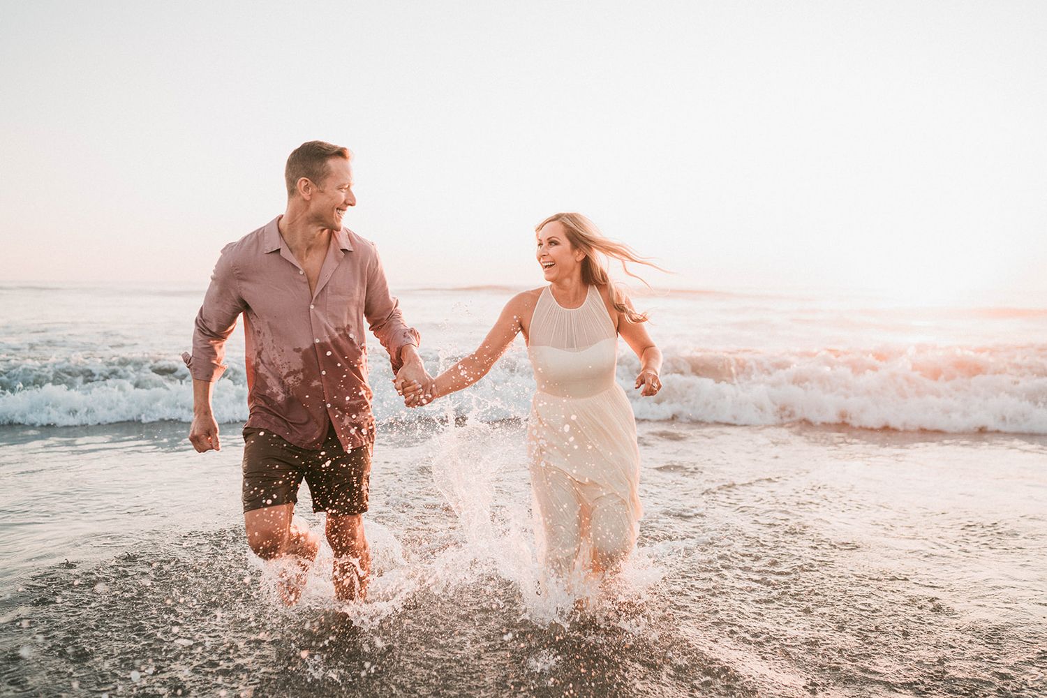 Joyful couple splashing and running through ocean water at sunset on a beach.