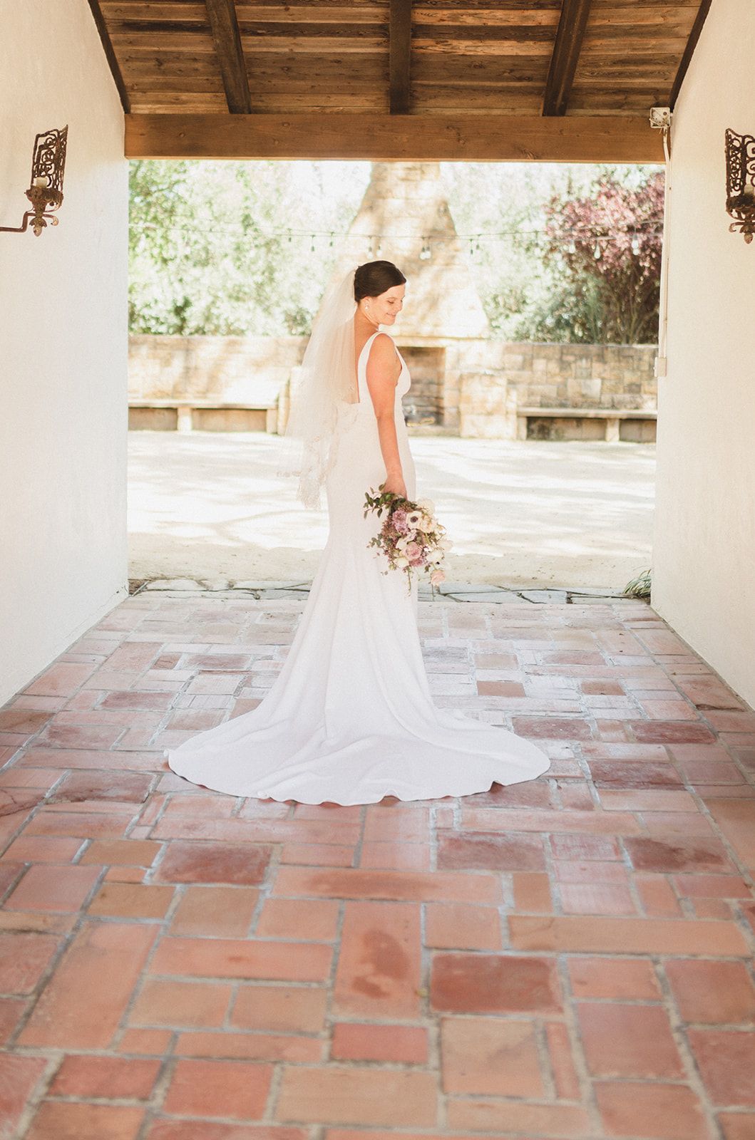 Wedding dress with long flowing train photographed in sequence on rustic terracotta tile patio under covered portico.