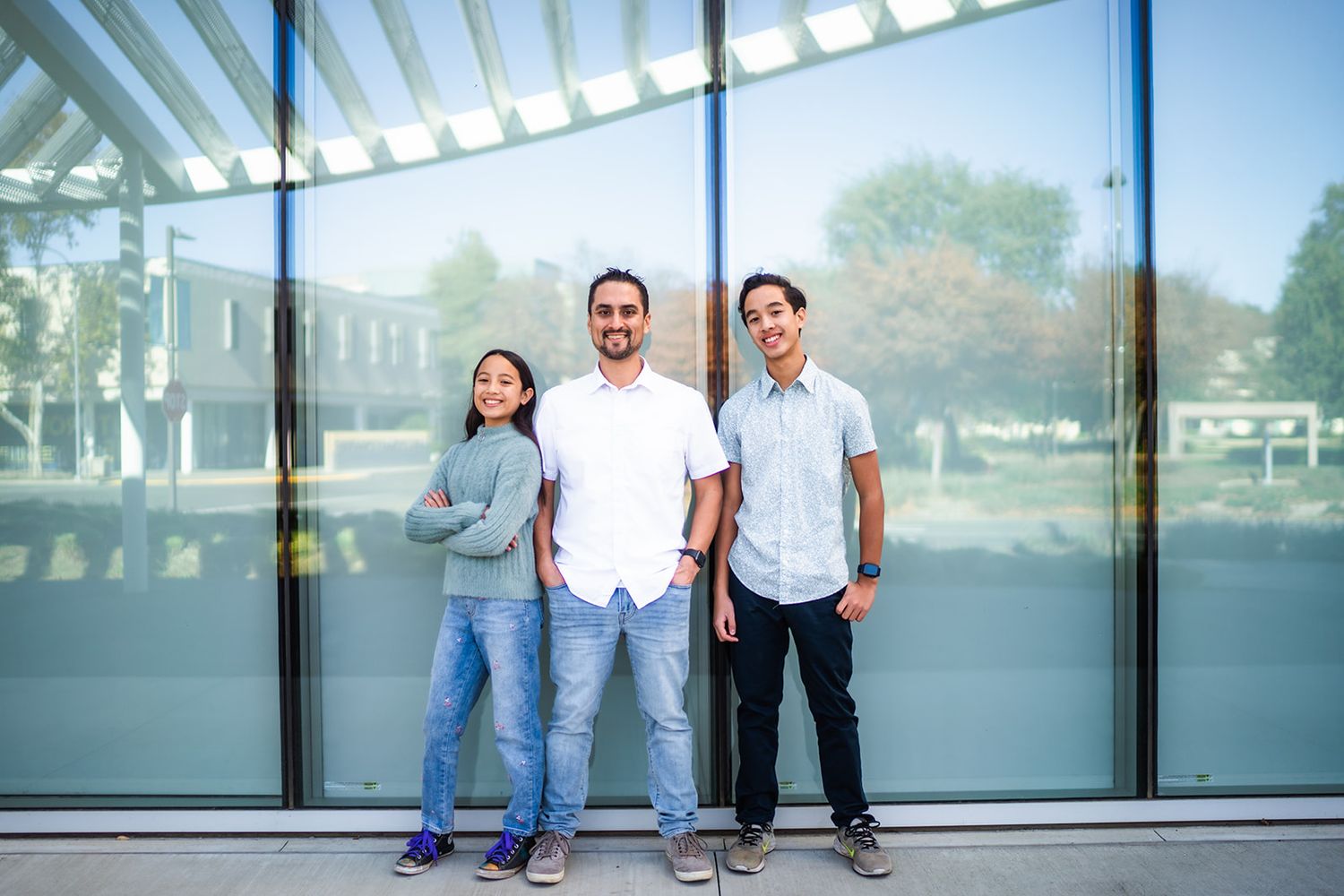 People pose against a modern glass wall with reflective surfaces in an architectural setting.