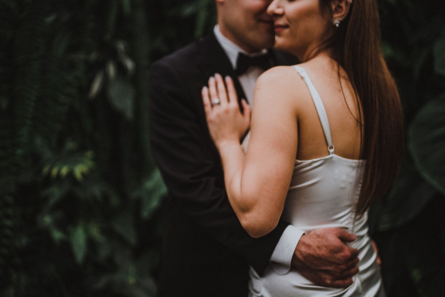 Tender moment between couple in dark moody lighting surrounded by foliage.