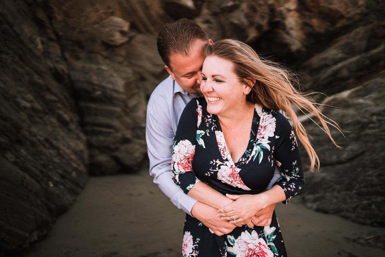 A couple embraces against dramatic rocky cliffs during a sunset photoshoot.