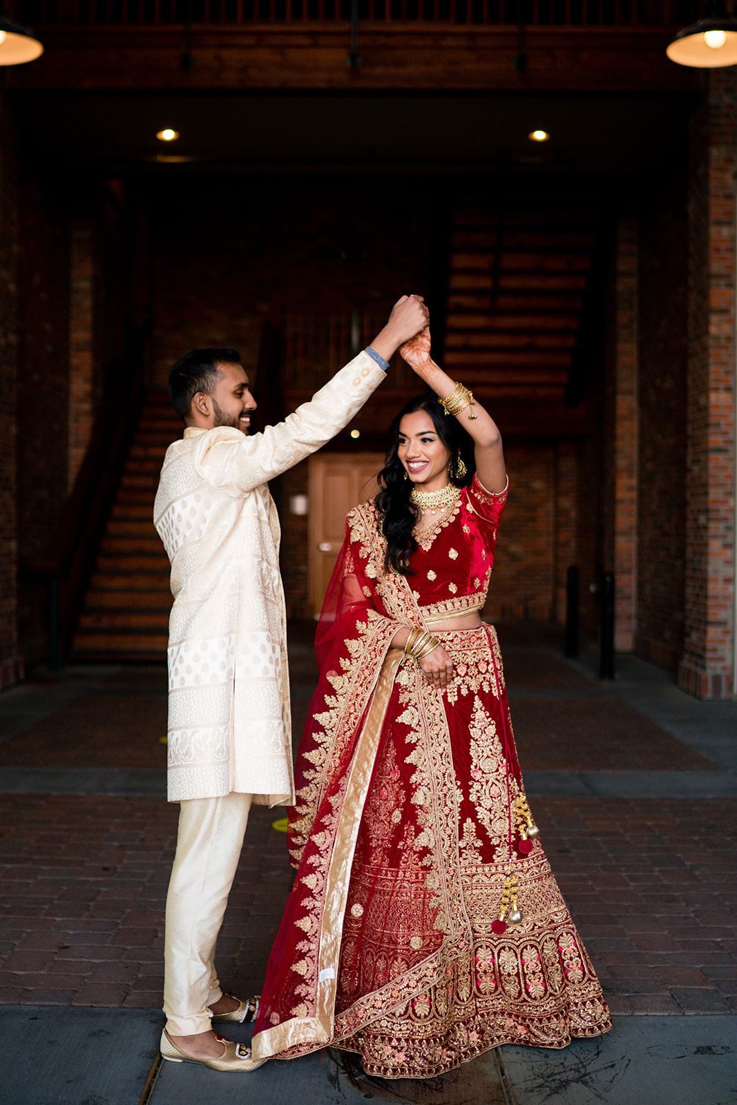 A couple dances together in traditional South Asian wedding attire inside a brick courtyard.