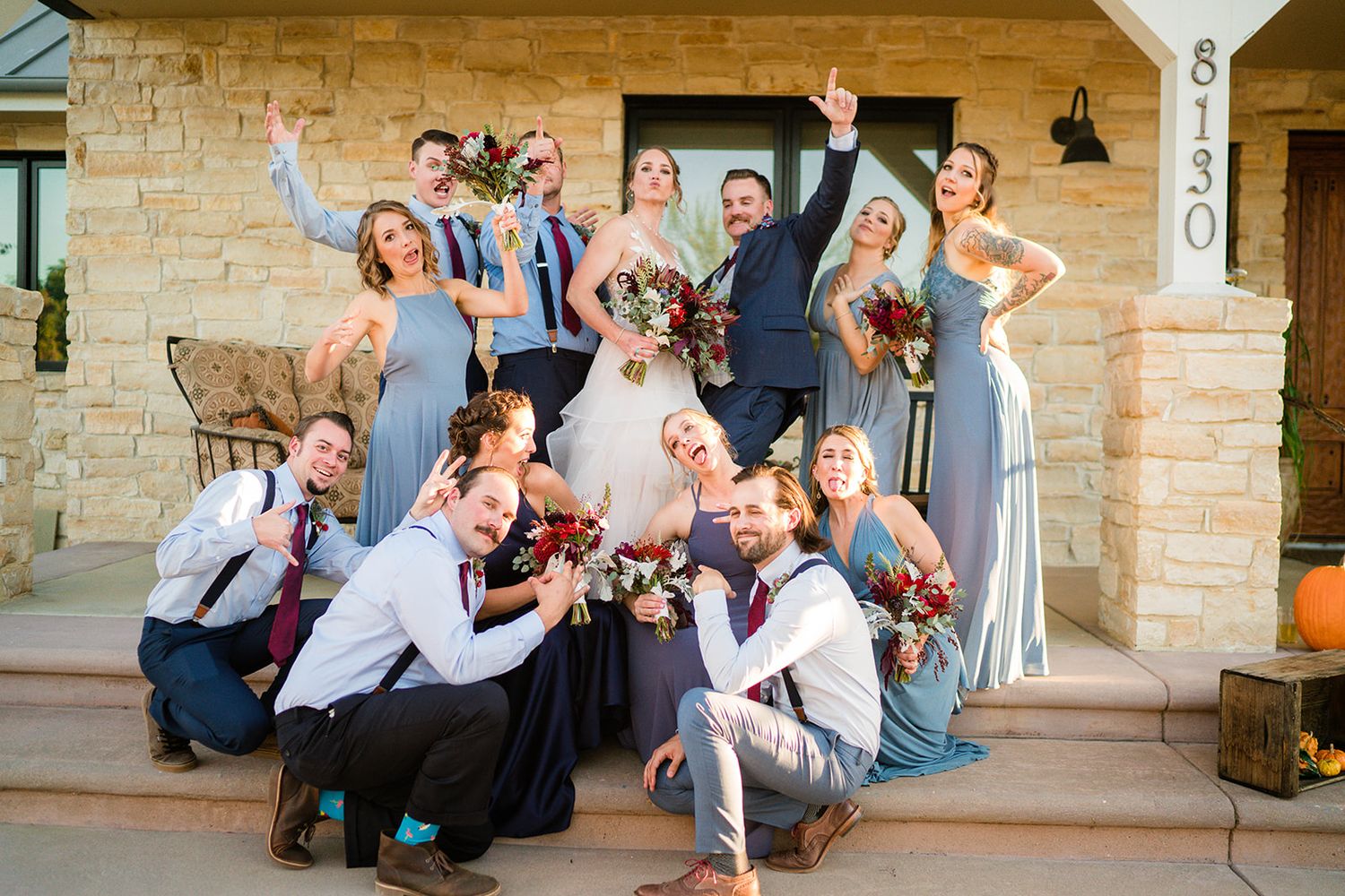 Wedding party poses together playfully on stone steps of venue.