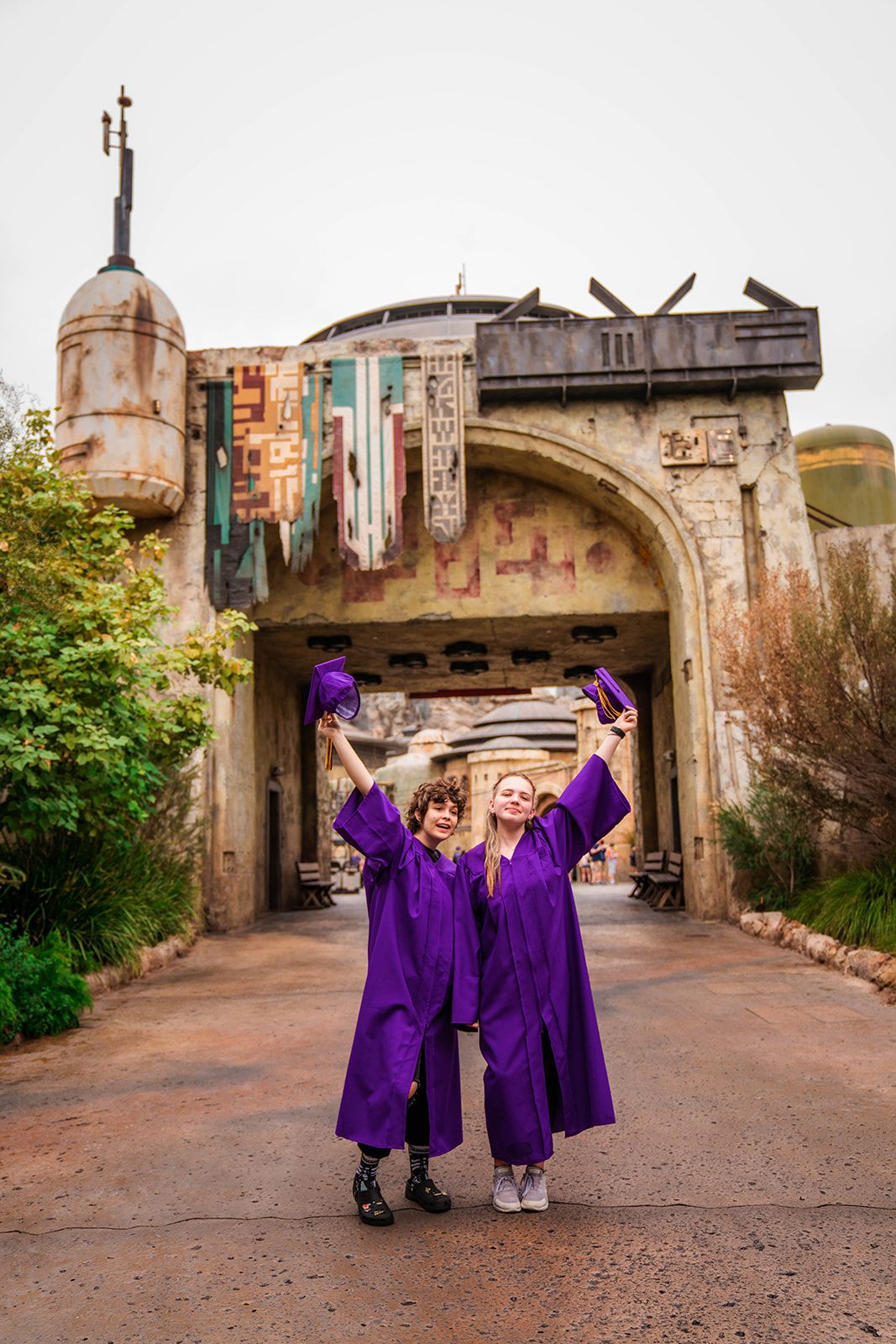Two graduates in purple caps and gowns celebrate at Star Wars Galaxy's Edge, Disneyland.