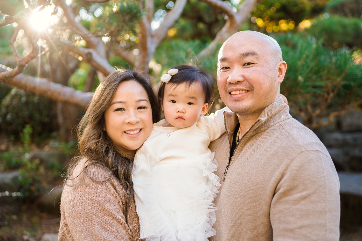 A family enjoys a candid moment together outdoors during sunset in a wooded garden setting.