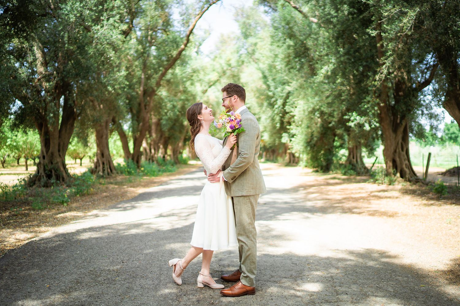 Bride and groom embracing on a tree-lined path outdoors on their wedding day.