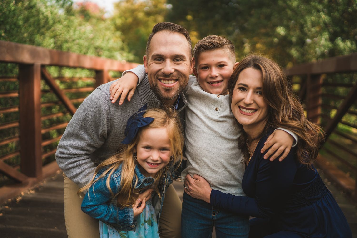 A joyful family portrait captured on a rustic wooden bridge surrounded by nature.