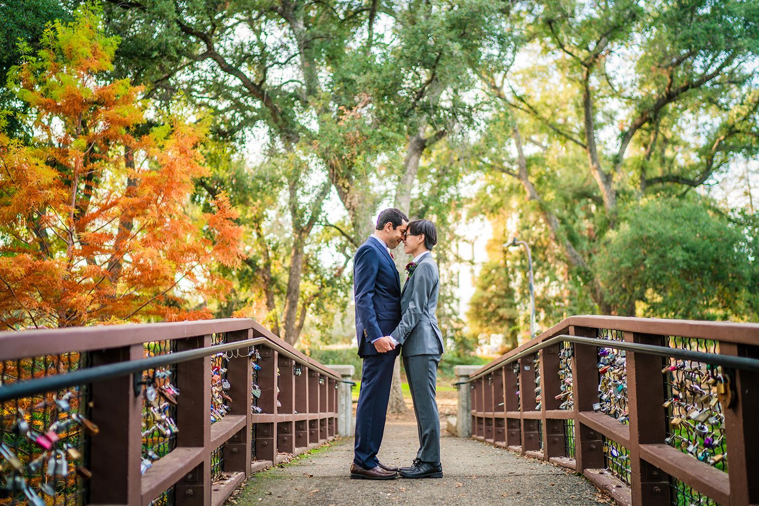 Wedding couple photographs on a wooden bridge surrounded by autumn foliage.