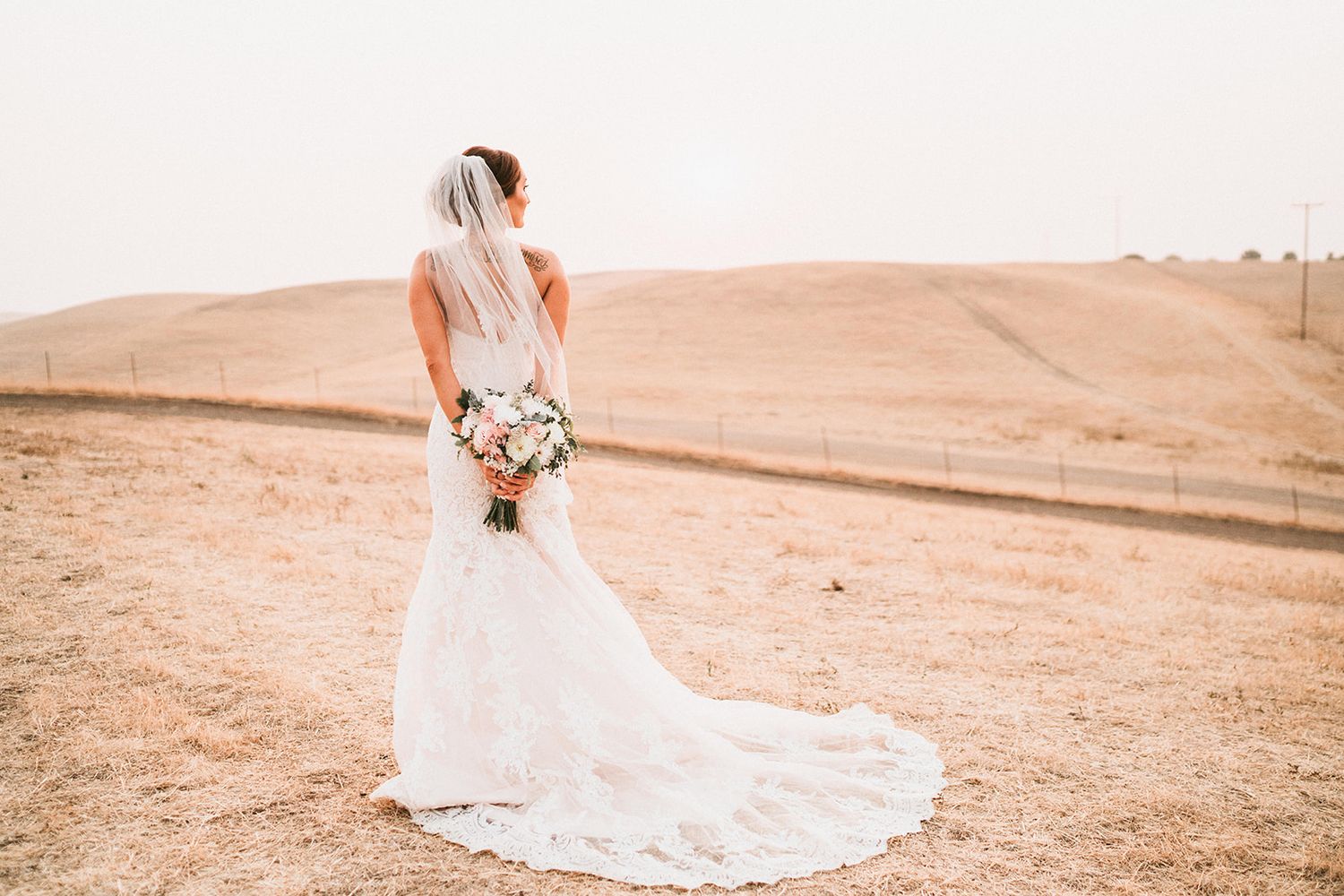 Bride in flowing white dress photographed against desert landscape at sunset.