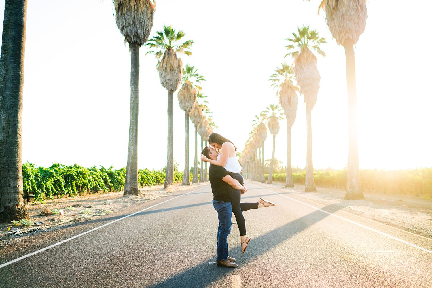 Couple walking along a palm tree lined path during golden hour.