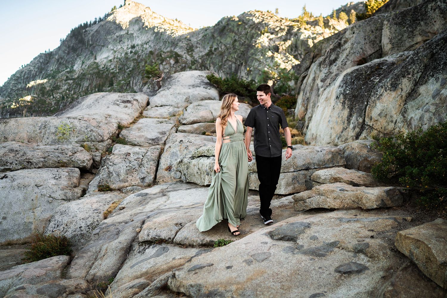 Couple walking hand in hand on rocky mountain terrain during sunset.