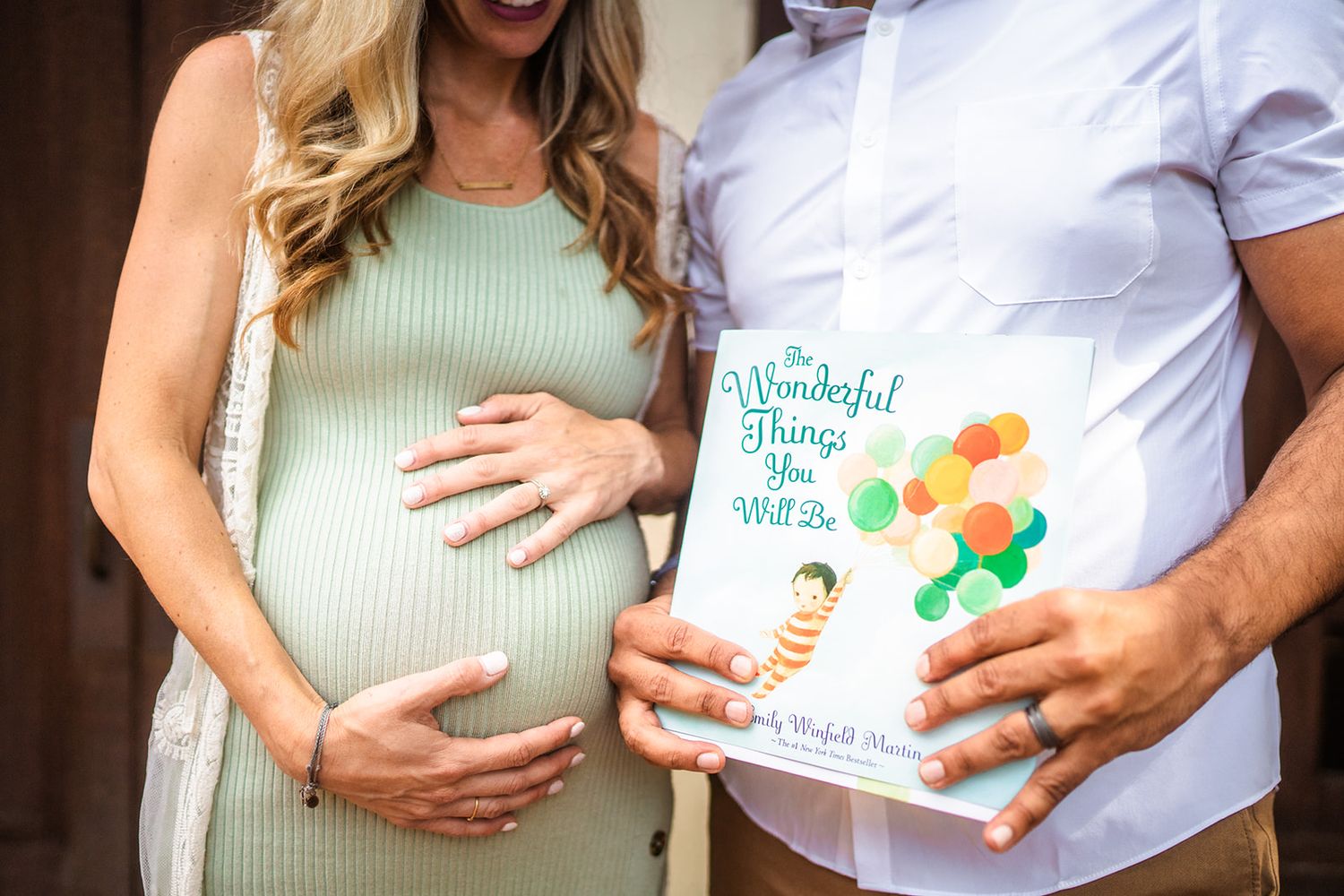 Pregnant woman in green dress holding baby book with partner during maternity photo shoot outdoors.