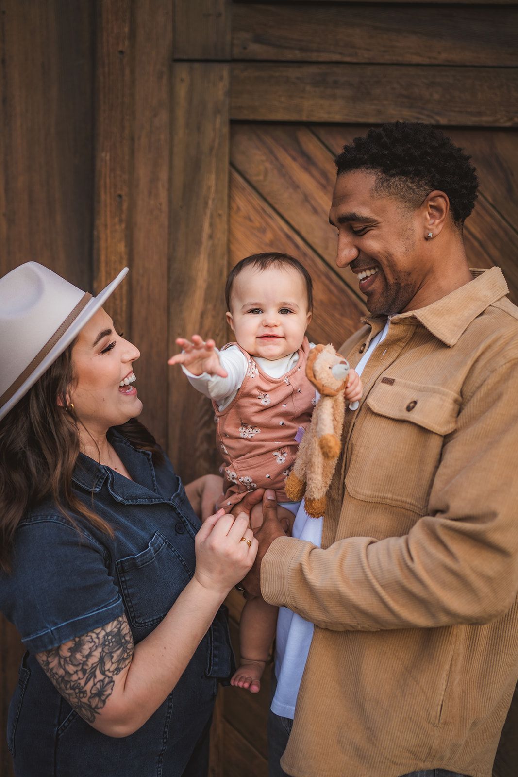 Happy family moment with baby in rustic setting against wooden barn door background.