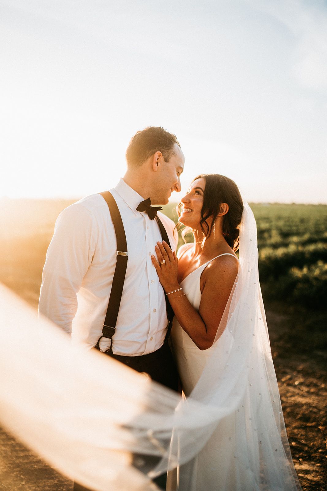 Romantic sunset portrait of newlyweds embracing in a field with golden light streaming through.