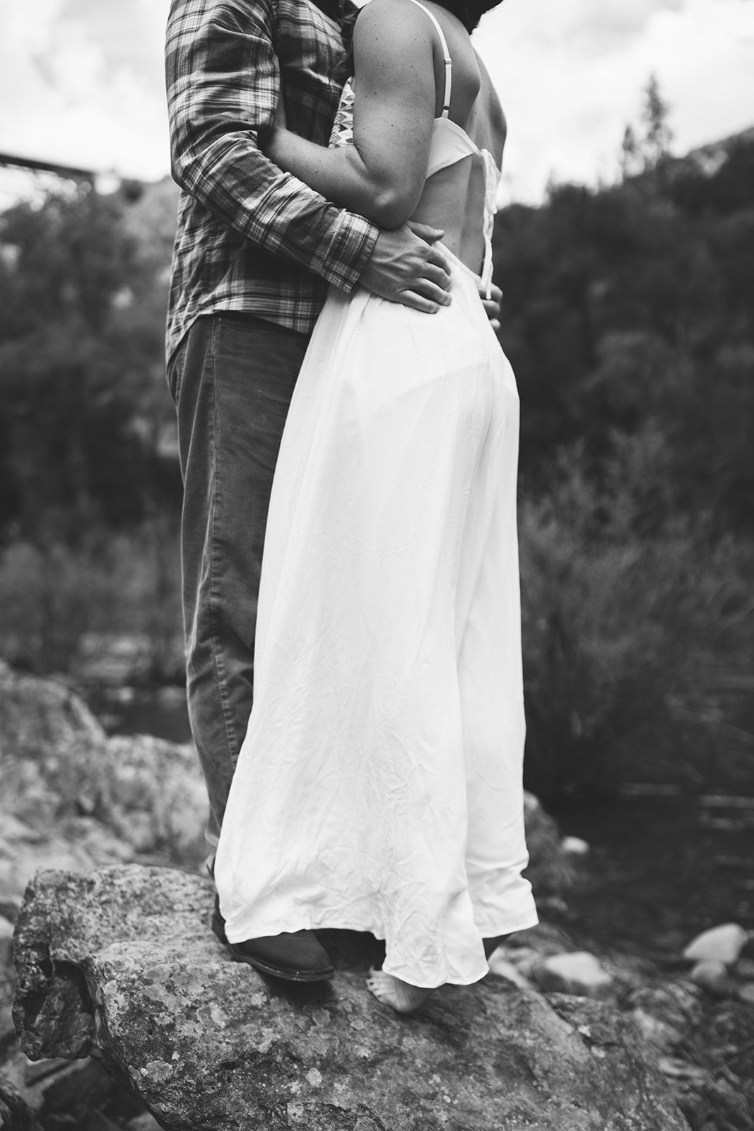 A romantic black and white portrait of a couple standing on rocks outdoors.
