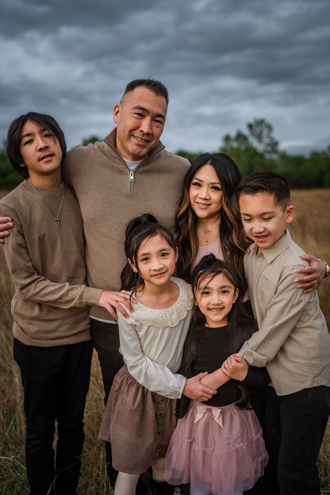 Family in coordinated neutral outfits posing together in a field under moody sky.