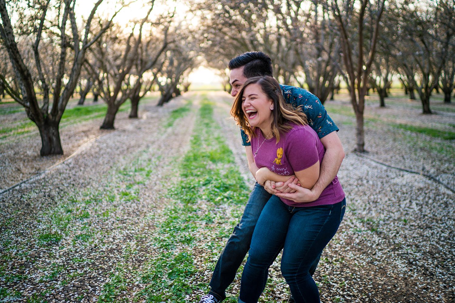 Couple playfully interacting in an almond orchard with blooming trees.