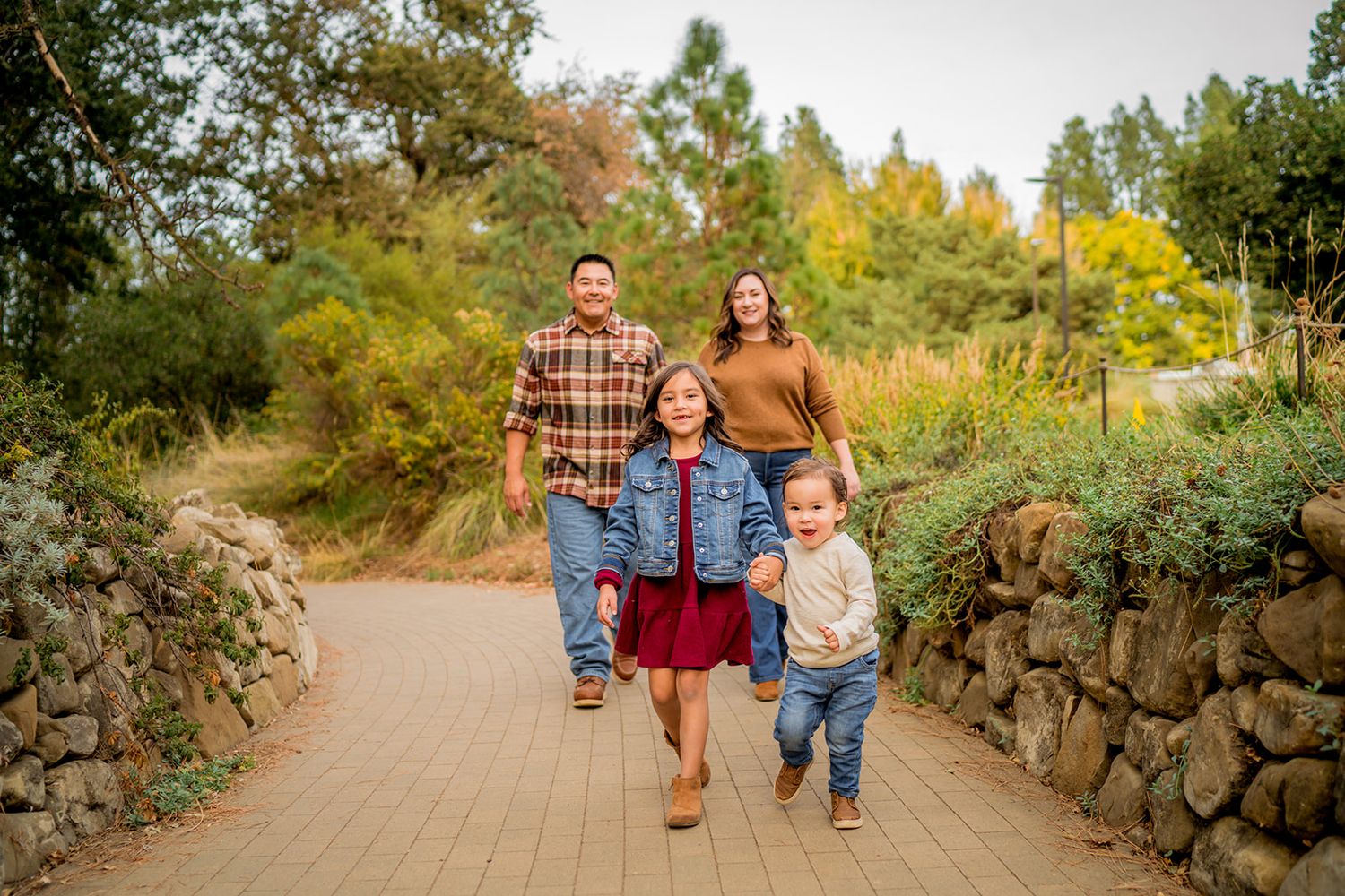 A group walks together on a stone-lined garden path surrounded by colorful autumn foliage on a sunny day.
