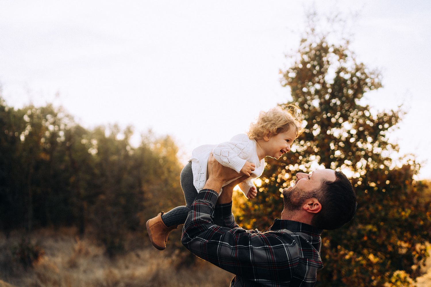 Silhouette of parent lifting child against golden sunset.