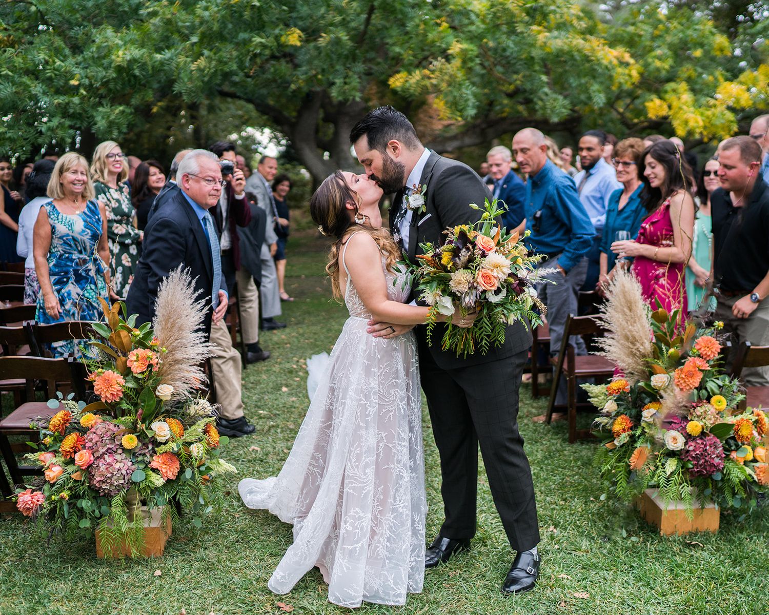 Outdoor garden wedding ceremony with colorful floral arrangements and gathered guests.