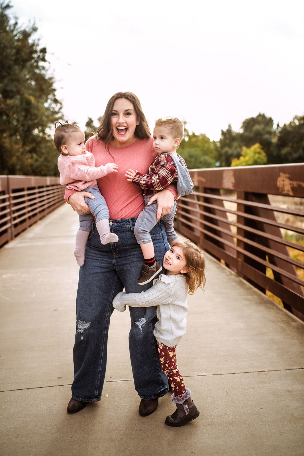 A joyful moment captured on a wooden bridge as family members embrace and laugh together in warm sunset lighting.
