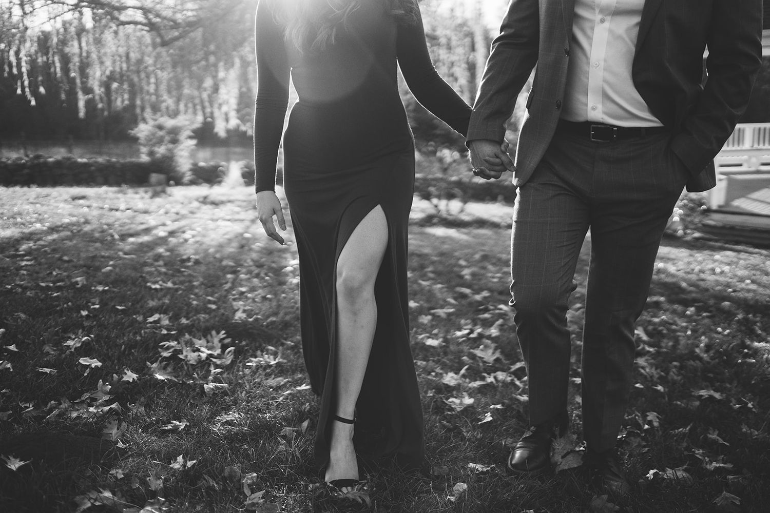 A couple embraces while standing in dappled sunlight among autumn leaves.
