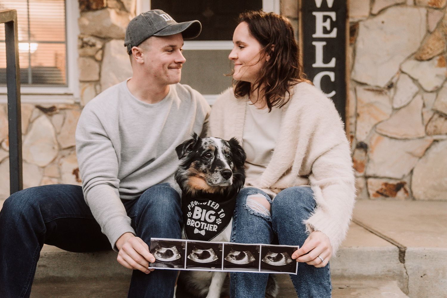 Couple sitting on steps with their border collie dog holding ultrasound photos and a big brother bandana for pregnancy announcement.