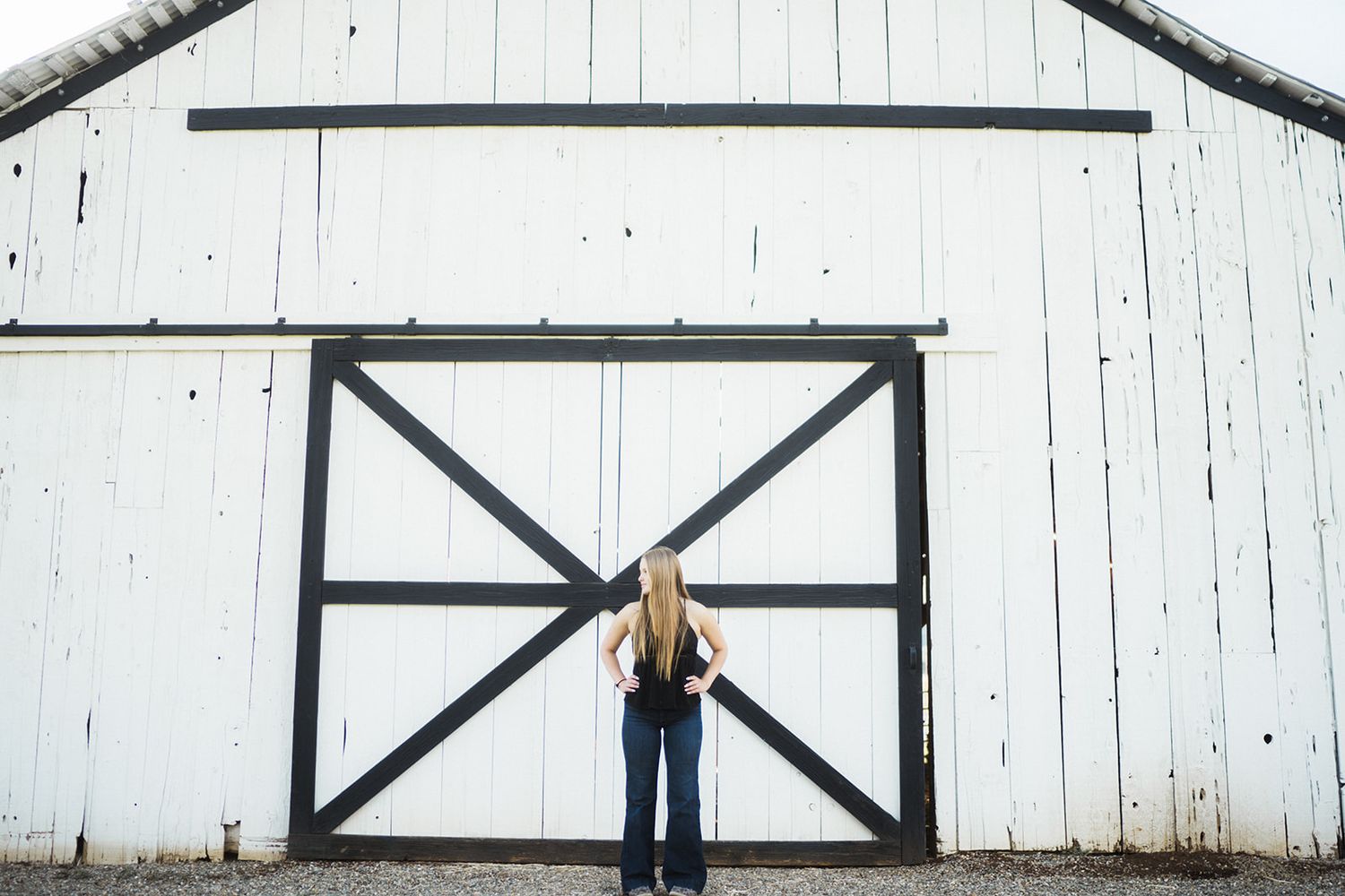 Woman with long blonde hair standing in front of a large white barn with black X-pattern sliding doors.