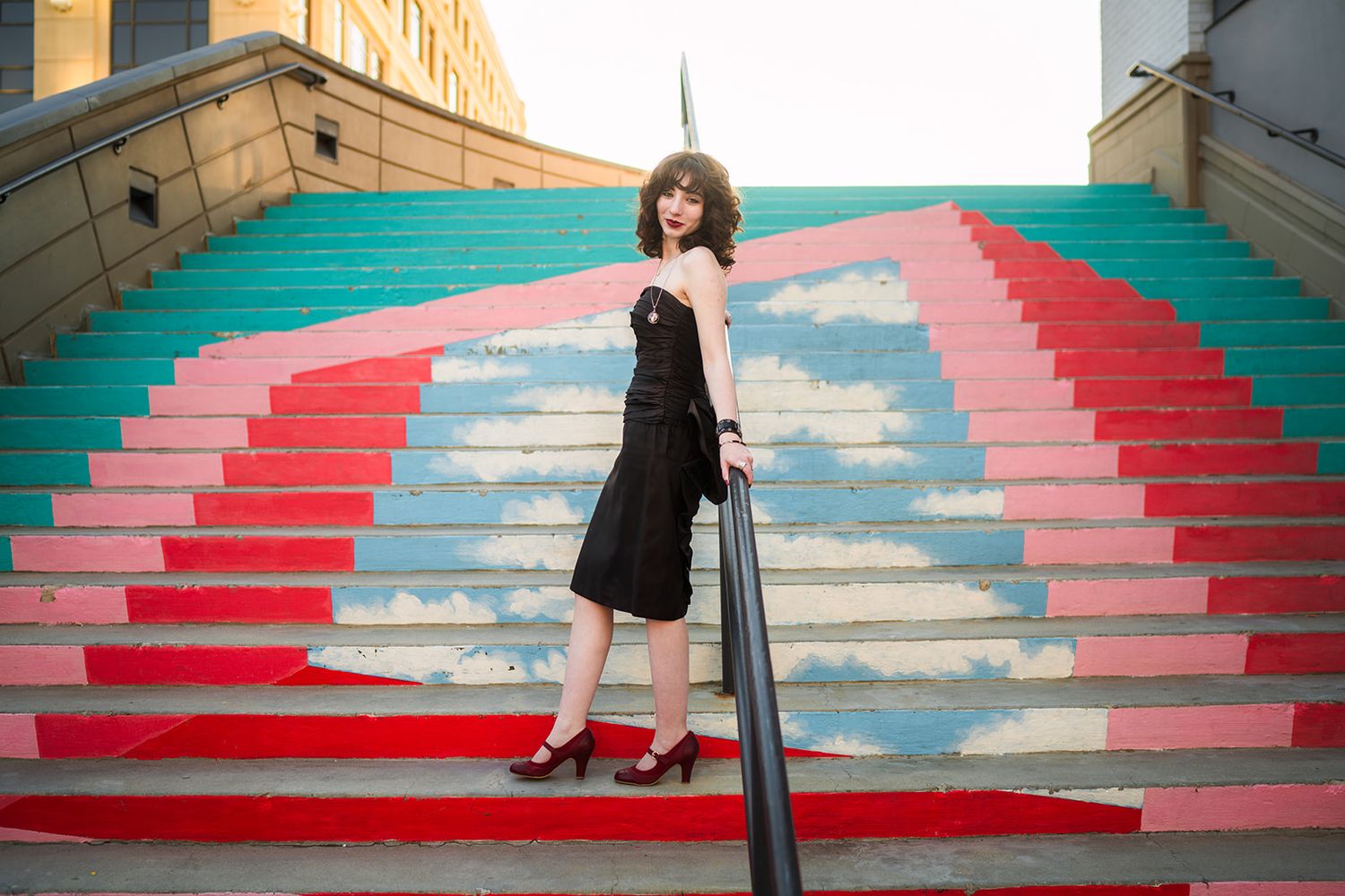 A series of whimsical photos on colorful stairs painted with cloud and sky motifs in pink, red and turquoise hues.