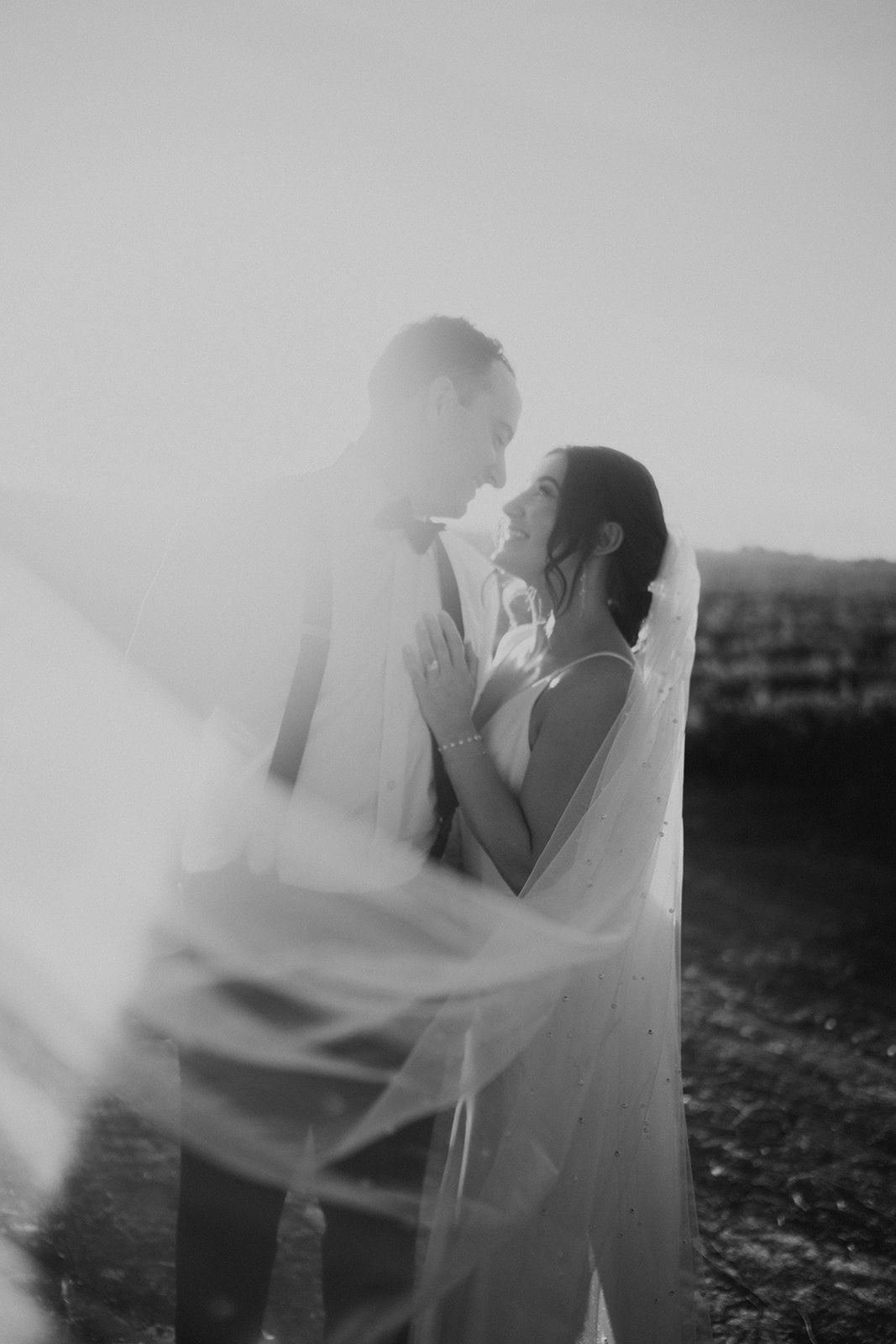 Ethereal black and white wedding portraits with flowing veil creating dreamy movement.