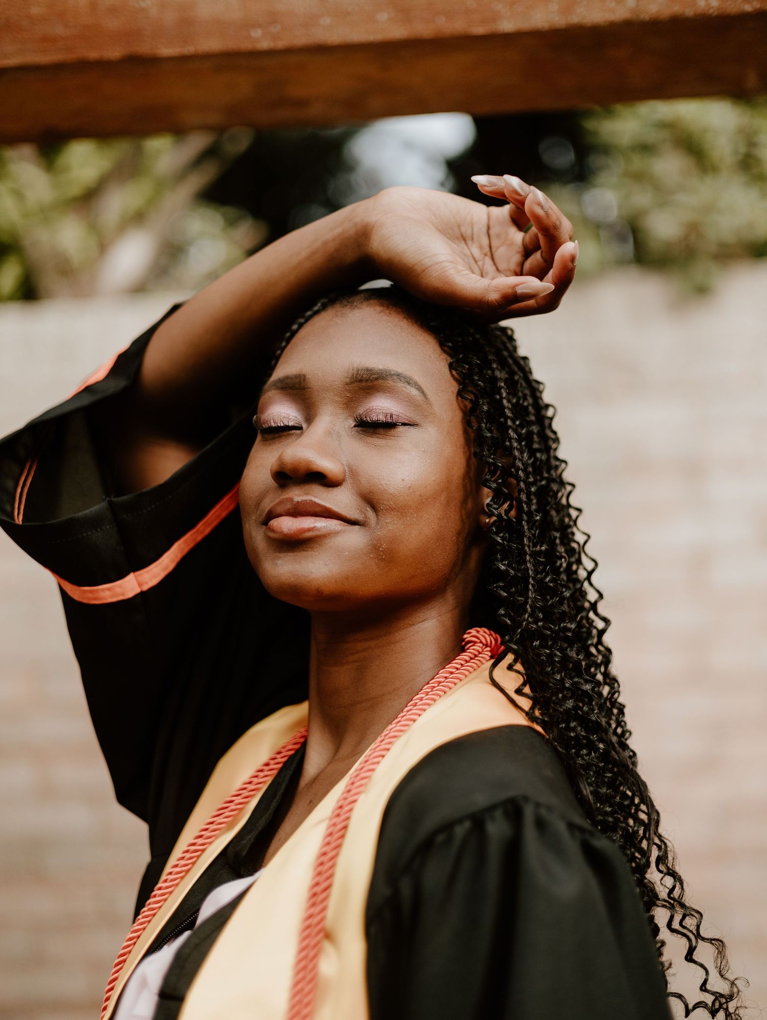 Artistic graduation portrait with decorative stole against natural background.