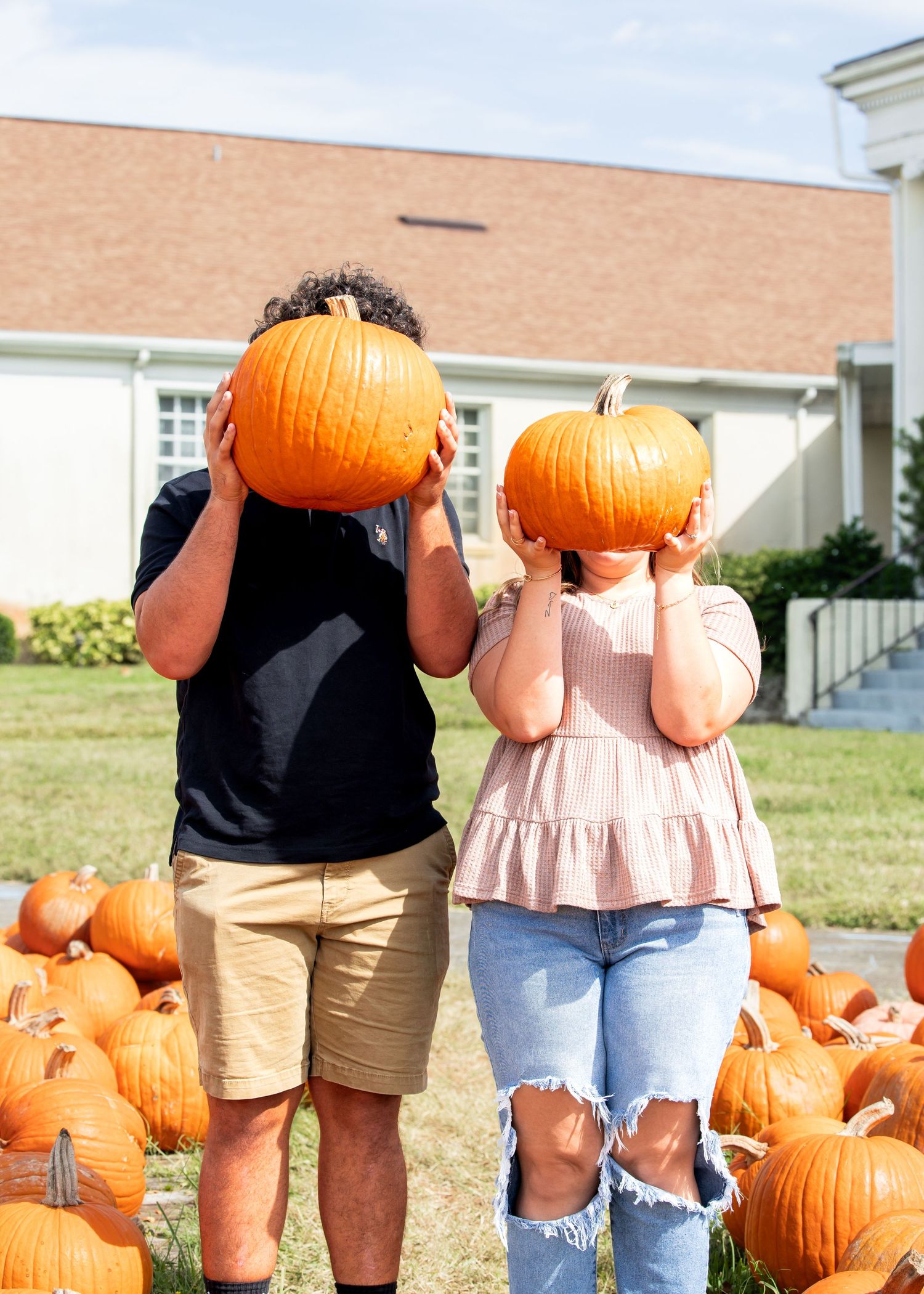 A group of people stand in a line outside while holding large orange pumpkins in their hands.