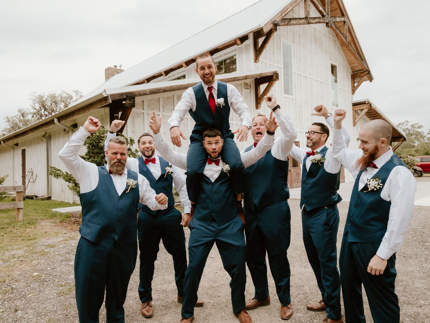 Wedding party in dark suits jumps joyfully in unison while posing for a candid outdoor photo session.