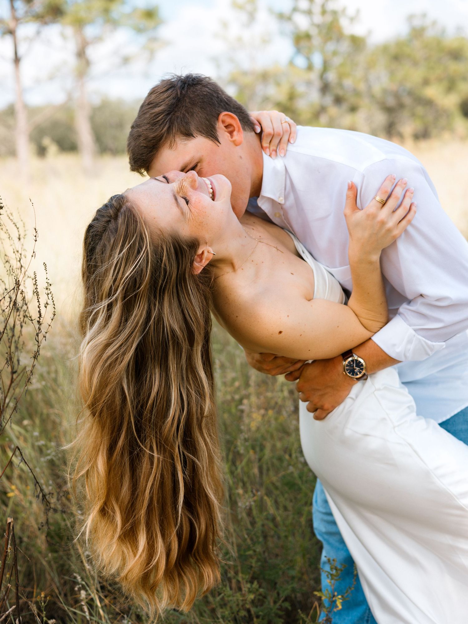 A romantic couple shares tender moments in a sunlit field with tall grass and natural lighting.
