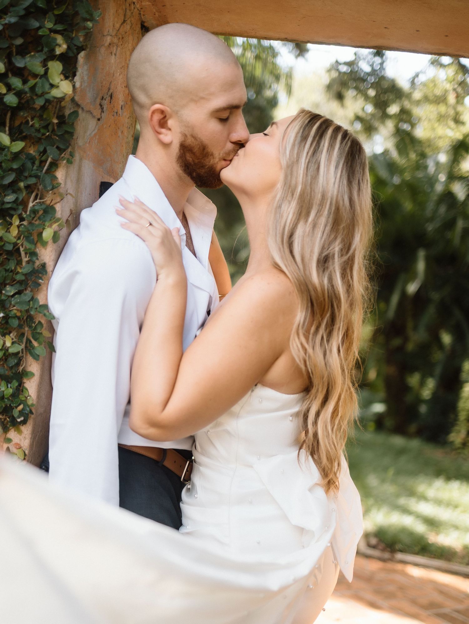 Intimate wedding moment under an ivy-covered archway in a garden setting.