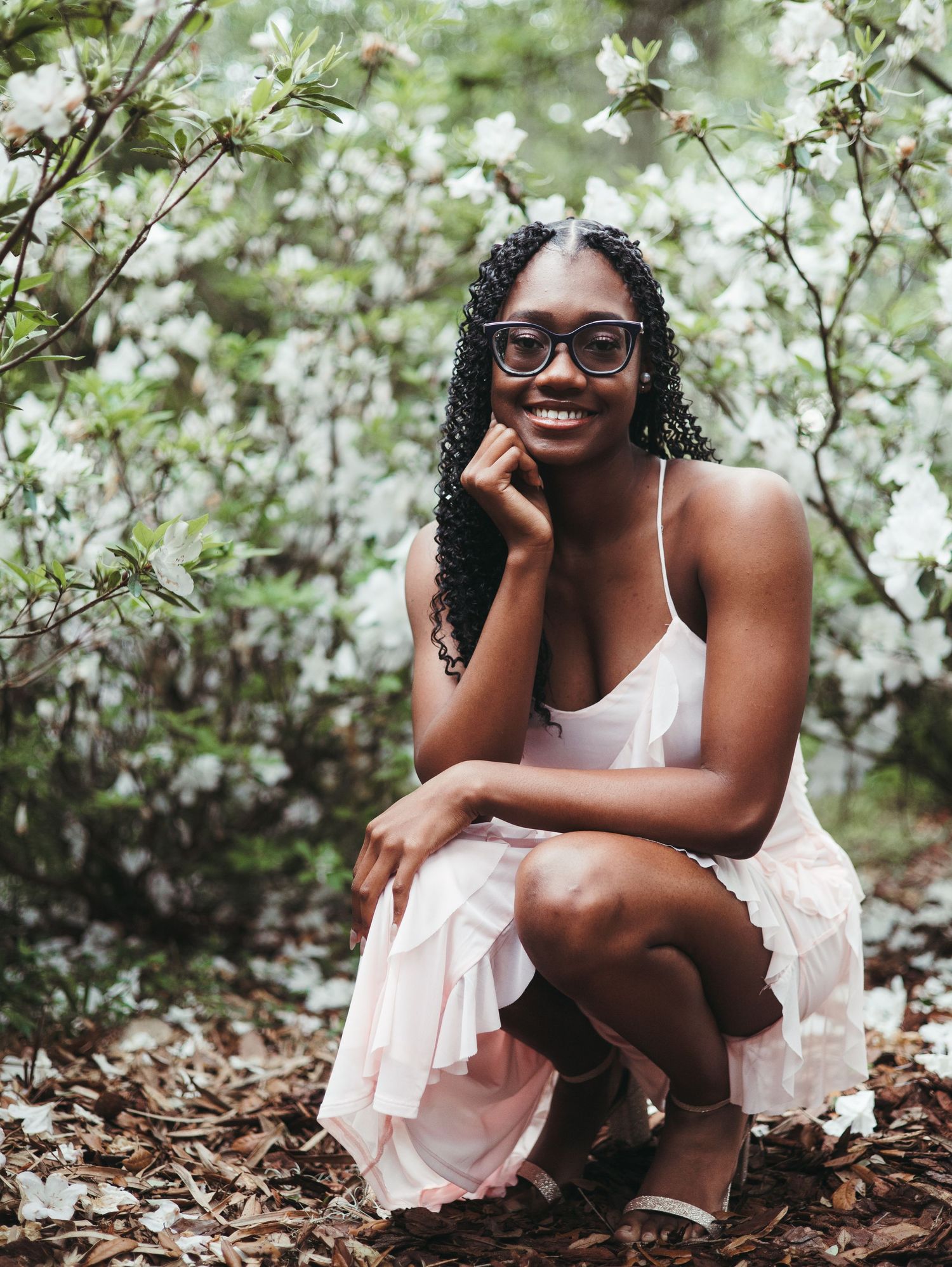 Graduate in white dress posing among blooming white flowers.