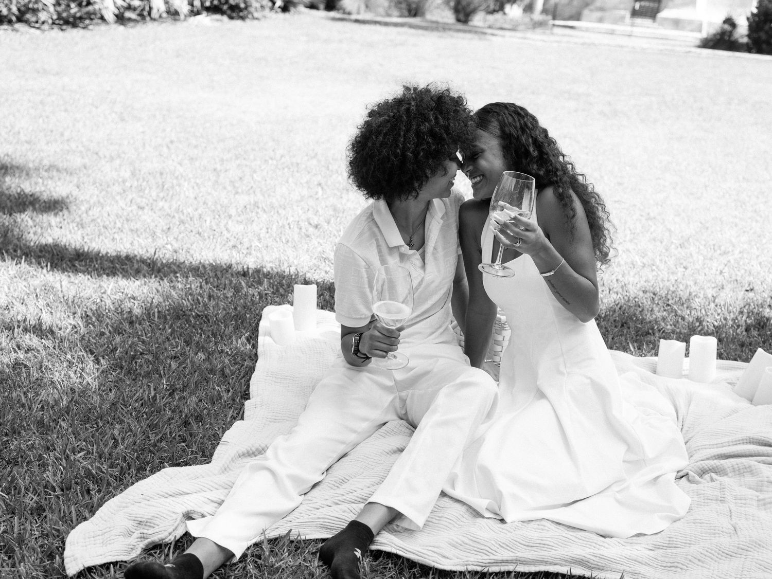 Intimate picnic moment on a white blanket with candles in an outdoor garden setting.