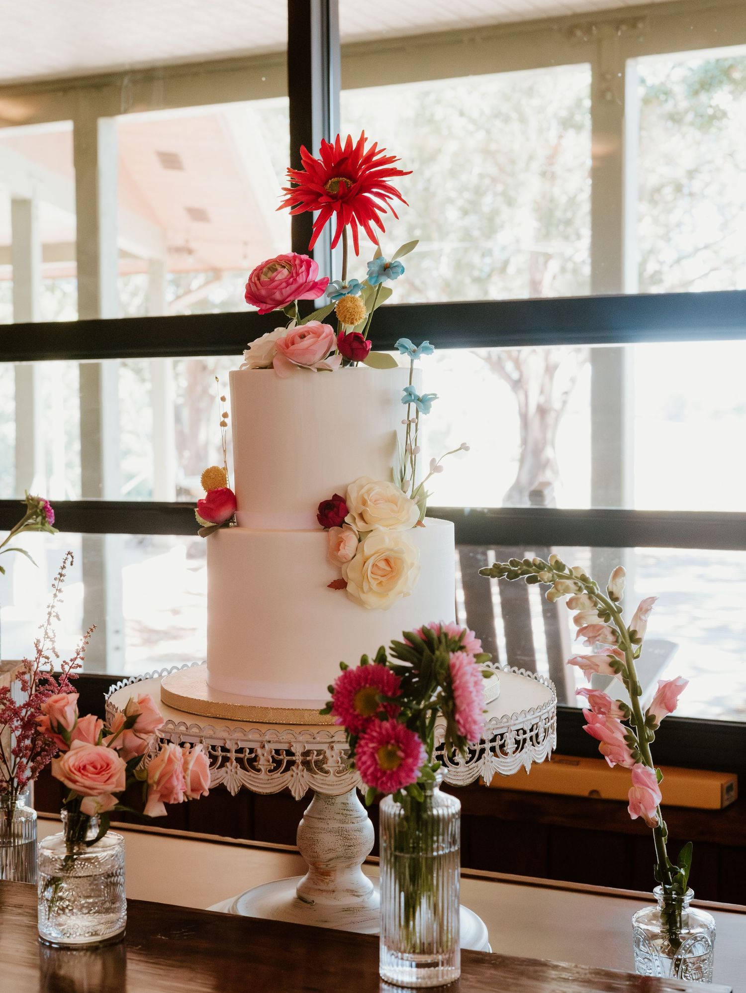 An elegant white wedding cake decorated with pink and red flowers displayed on a wooden table.