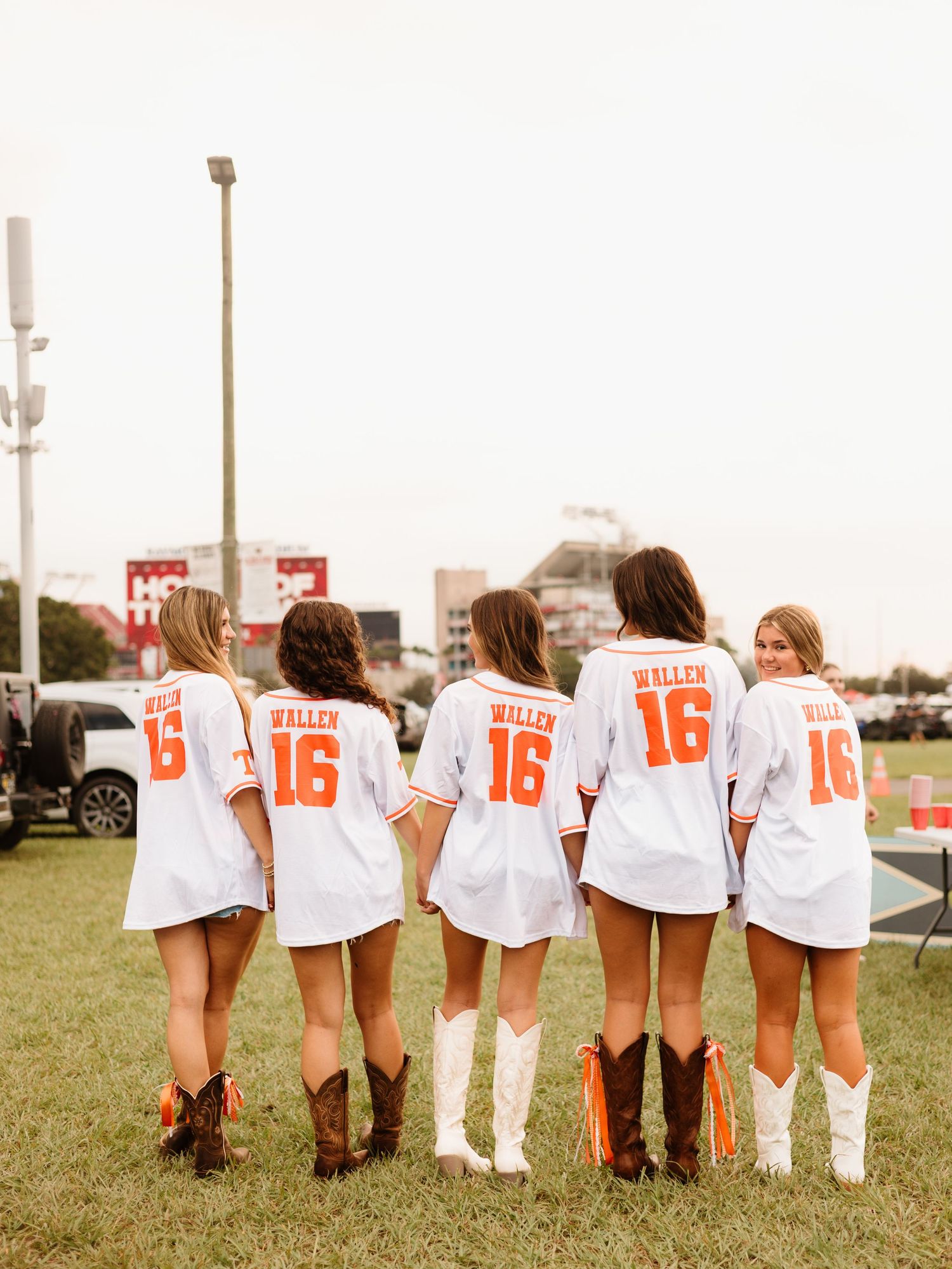 A row of soccer players wearing matching white jerseys with numbers stand with their backs to the camera on a grass field.