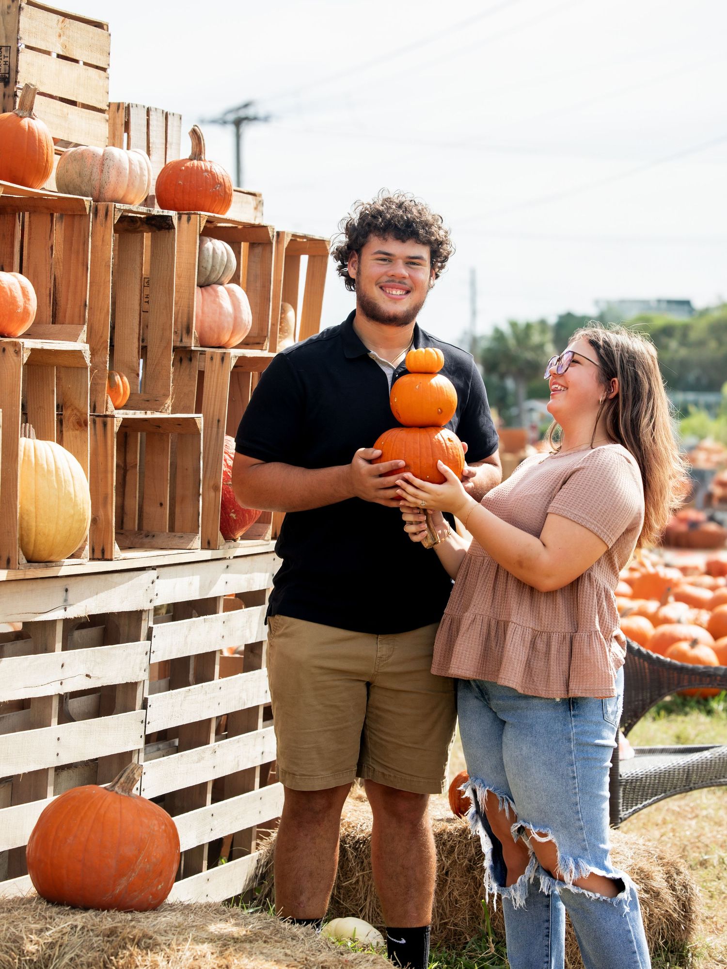 Couple enjoying a fall day at a rustic pumpkin patch with wooden crates and orange pumpkins in the background.