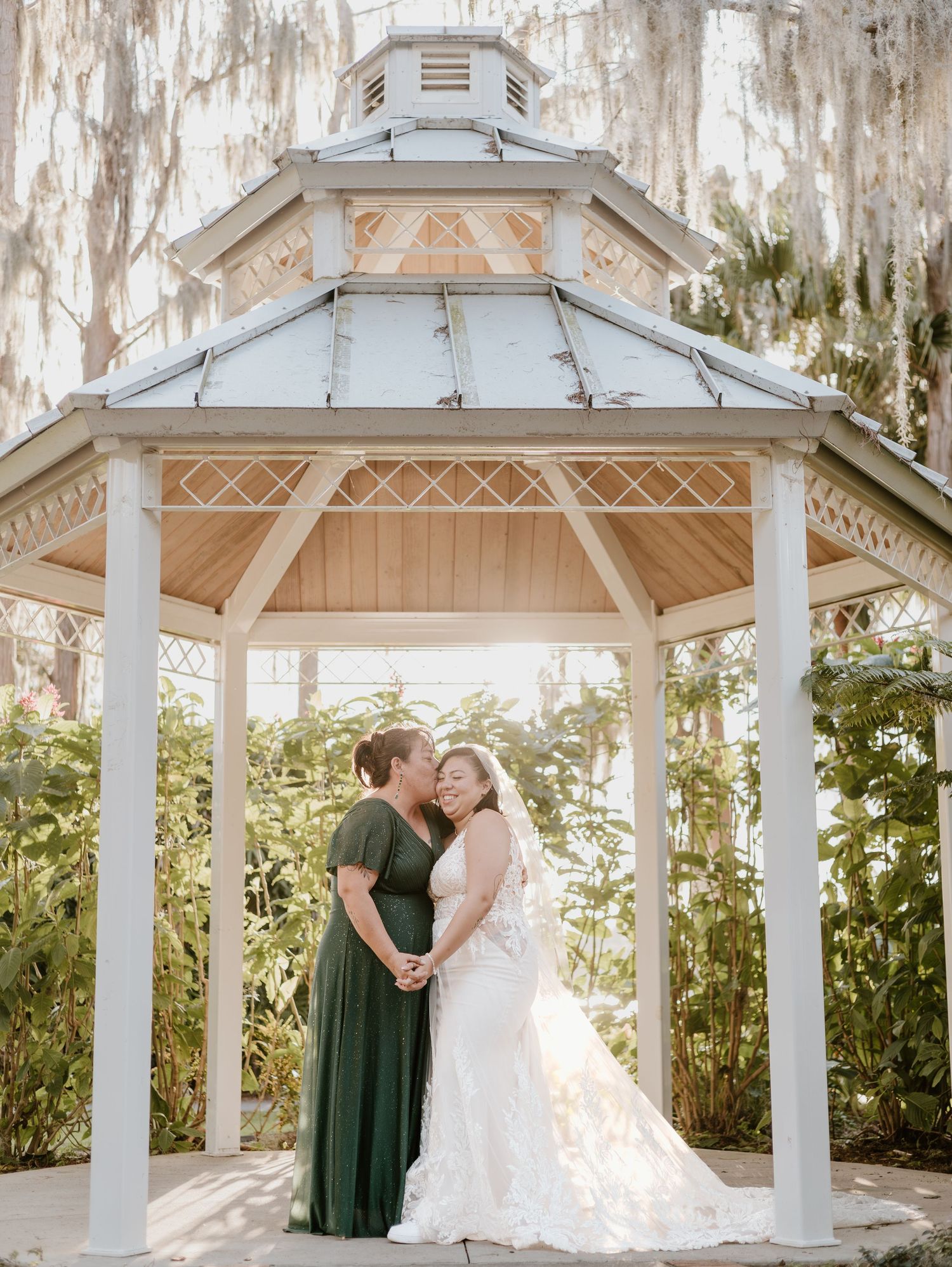 A romantic scene at a white gazebo in a garden setting with spanish moss draped trees in the background.