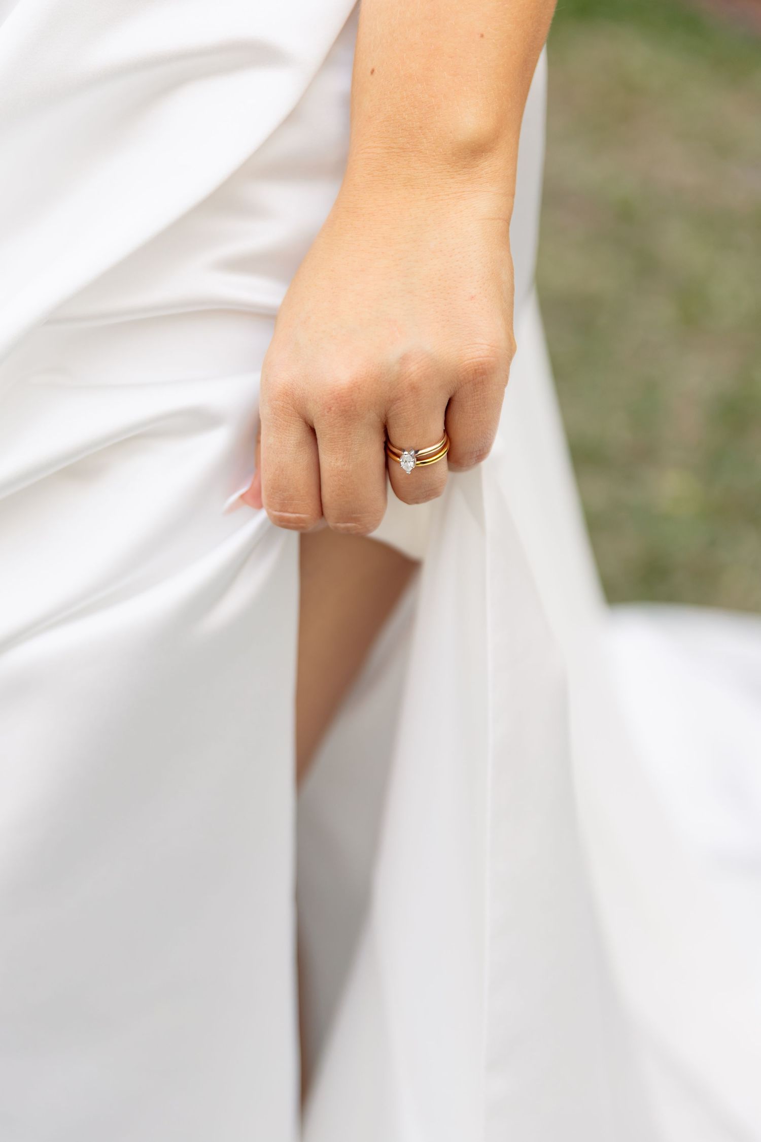 Close-up of a bride's hand holding her white wedding dress, showcasing a delicate gold diamond engagement ring.