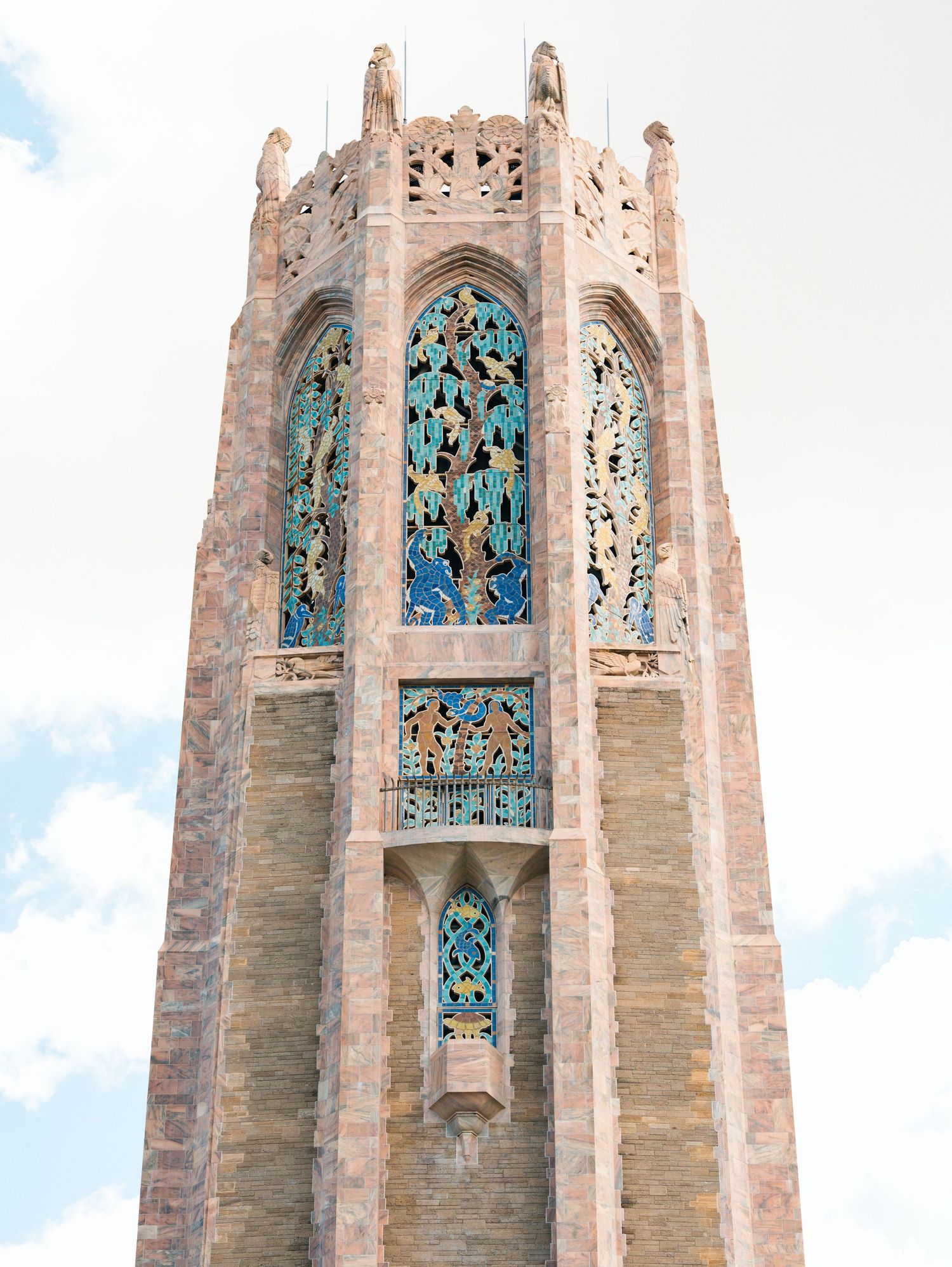 A tall Gothic church tower with ornate turquoise stained glass windows and limestone details against a bright sky.