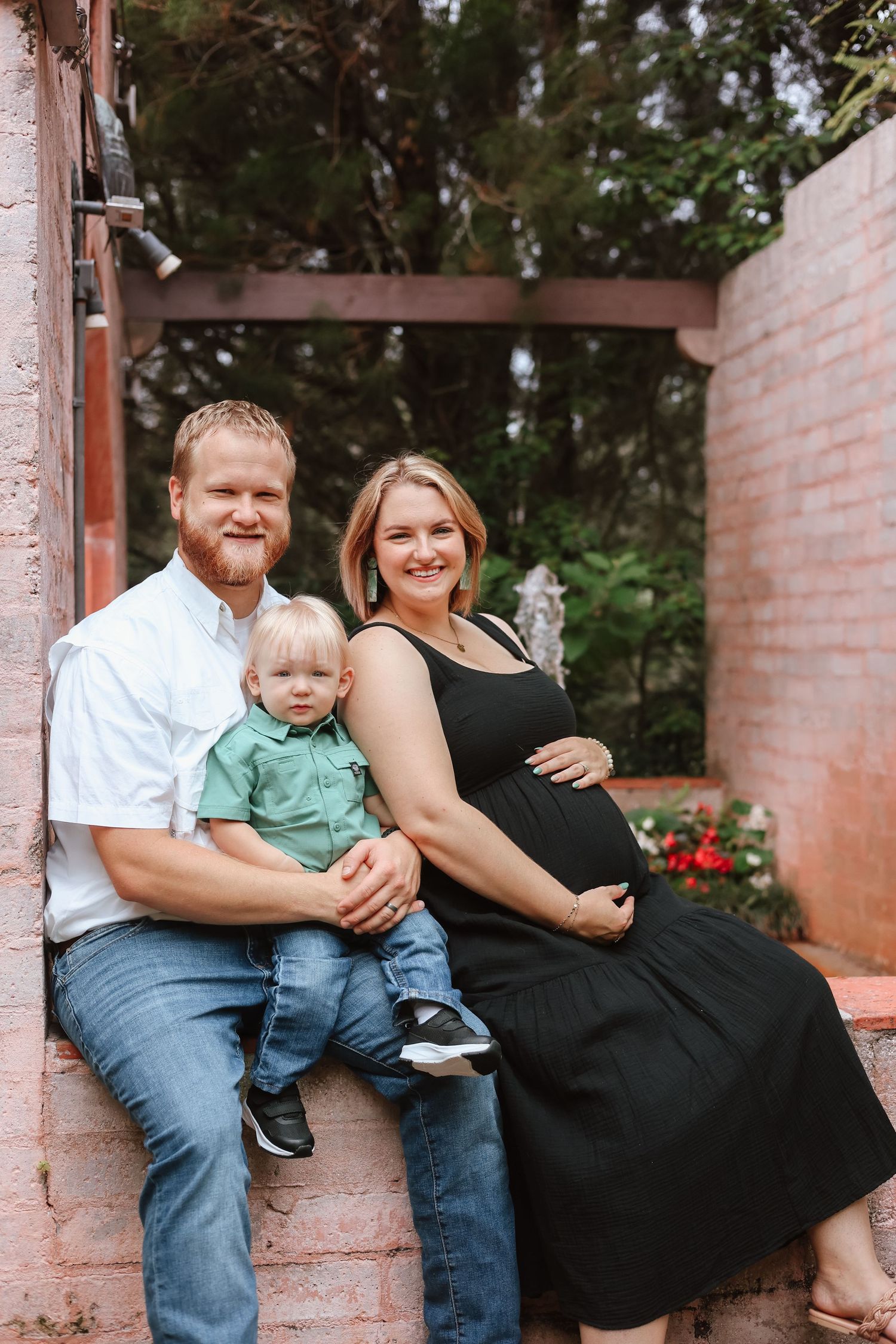 Family wearing black and denim sitting together on pink brick columns outdoors in a garden setting.