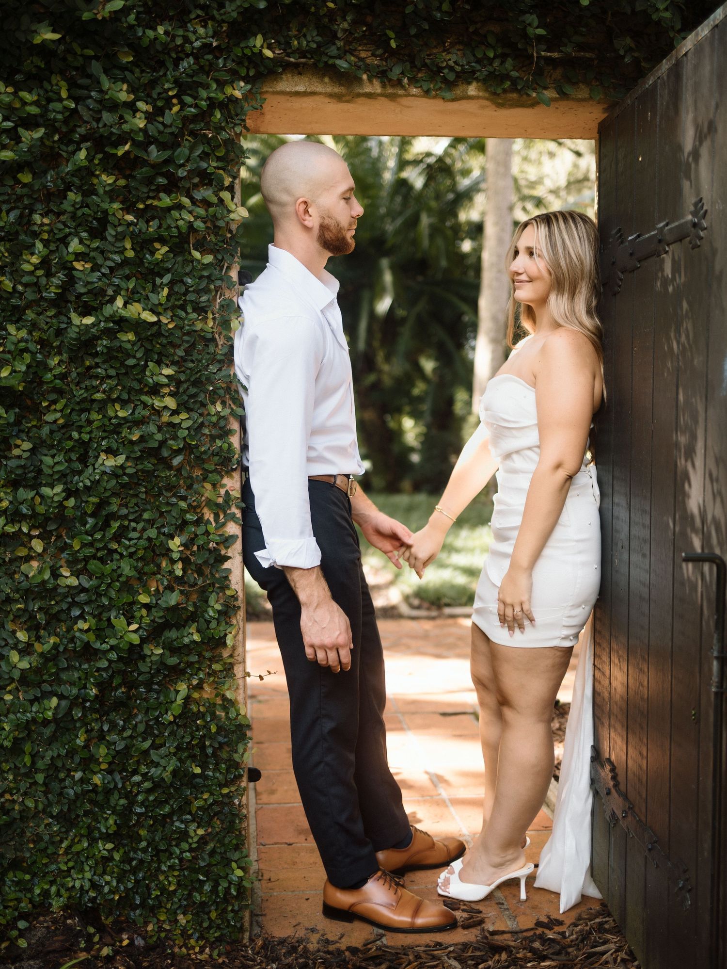 Romantic engagement photo series showing a white dress and cowboy boots with ivy covered brick wall in background.